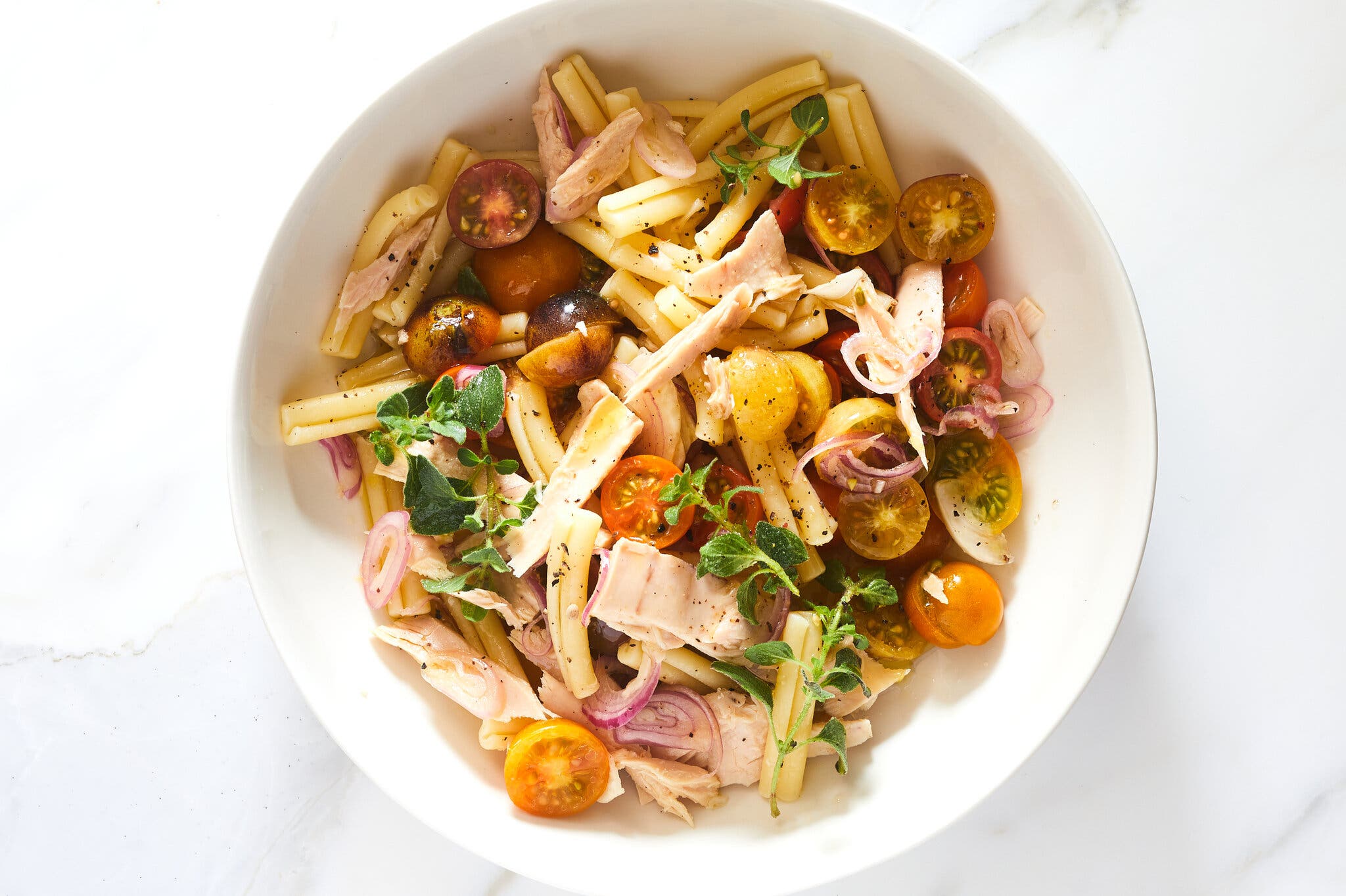 An overhead image of pasta, tuna and tomatoes in a white bowl.