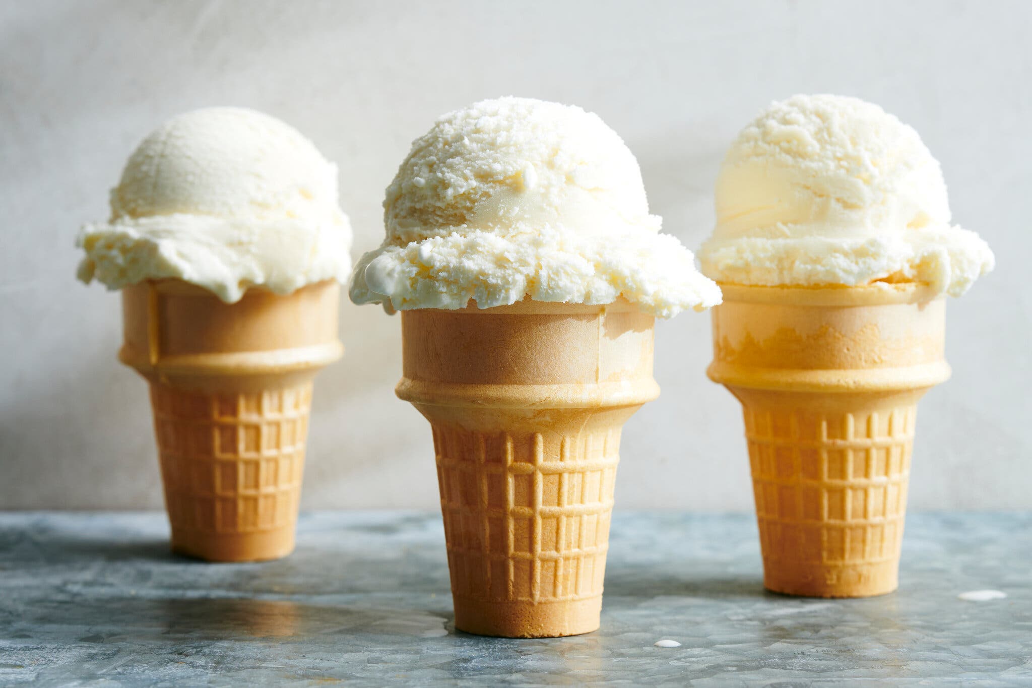 Three cake cones are topped with scoops of vanilla ice cream.