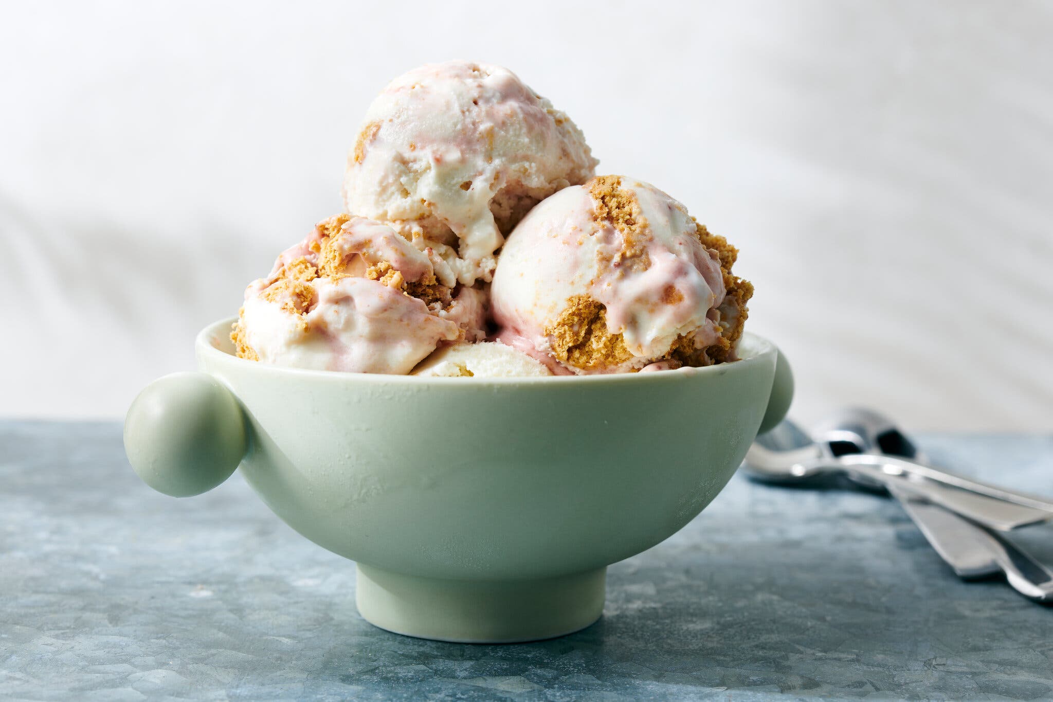 A pale green bowl is filled with scoops of strawberry cheesecake ice cream.