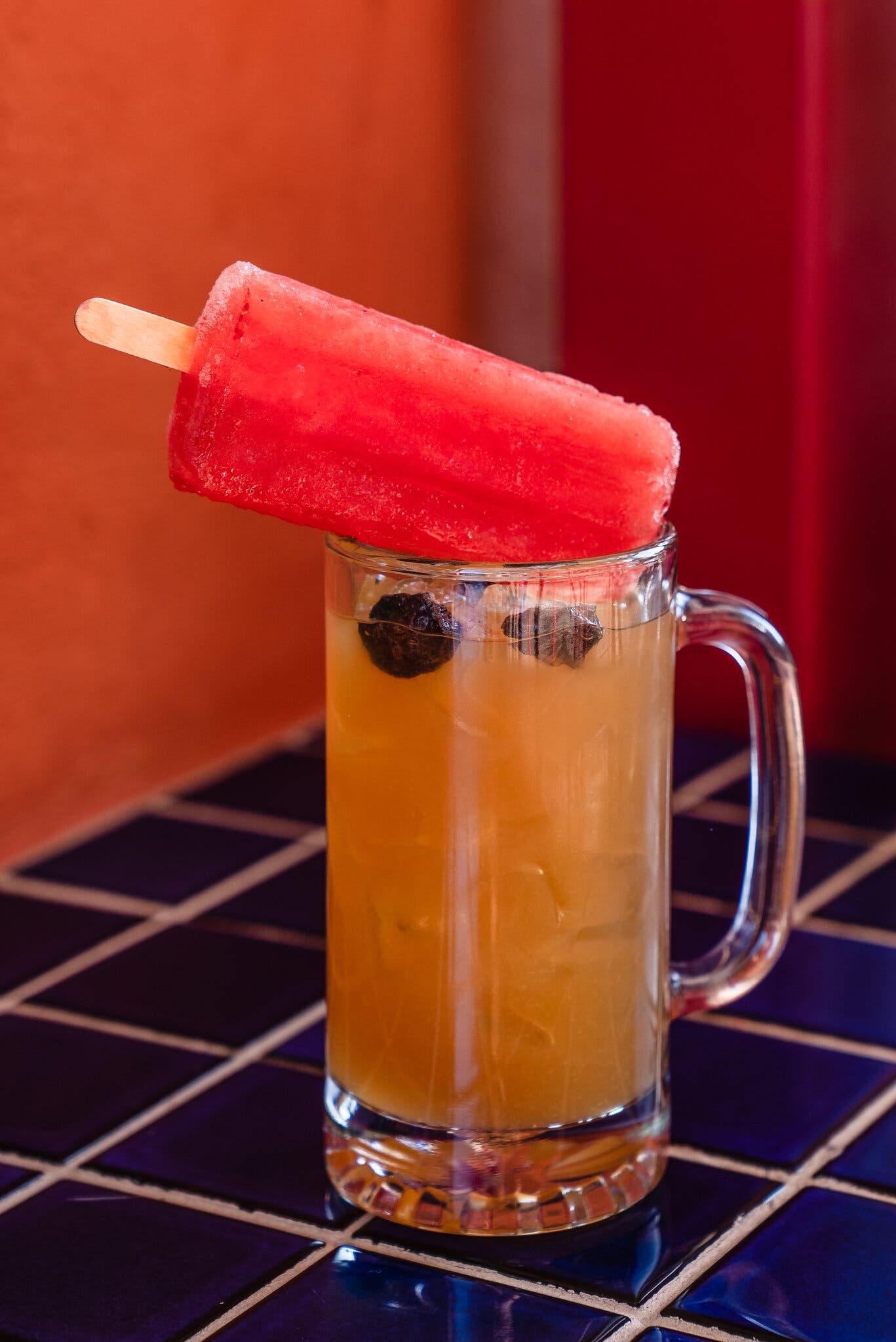 A fuschia paleta rests on top of a stein glass filled with a cocktail.