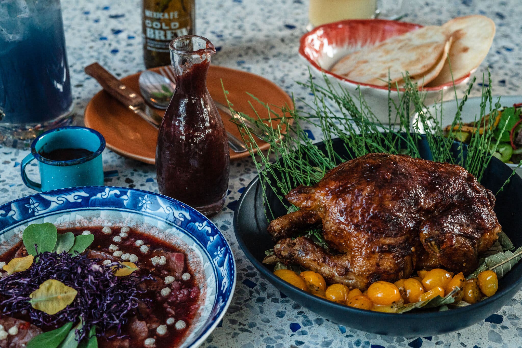 A platter of roasted Cornish hen and a plate of steak covered in sauce sit next to a carafe of chamoy sauce.
