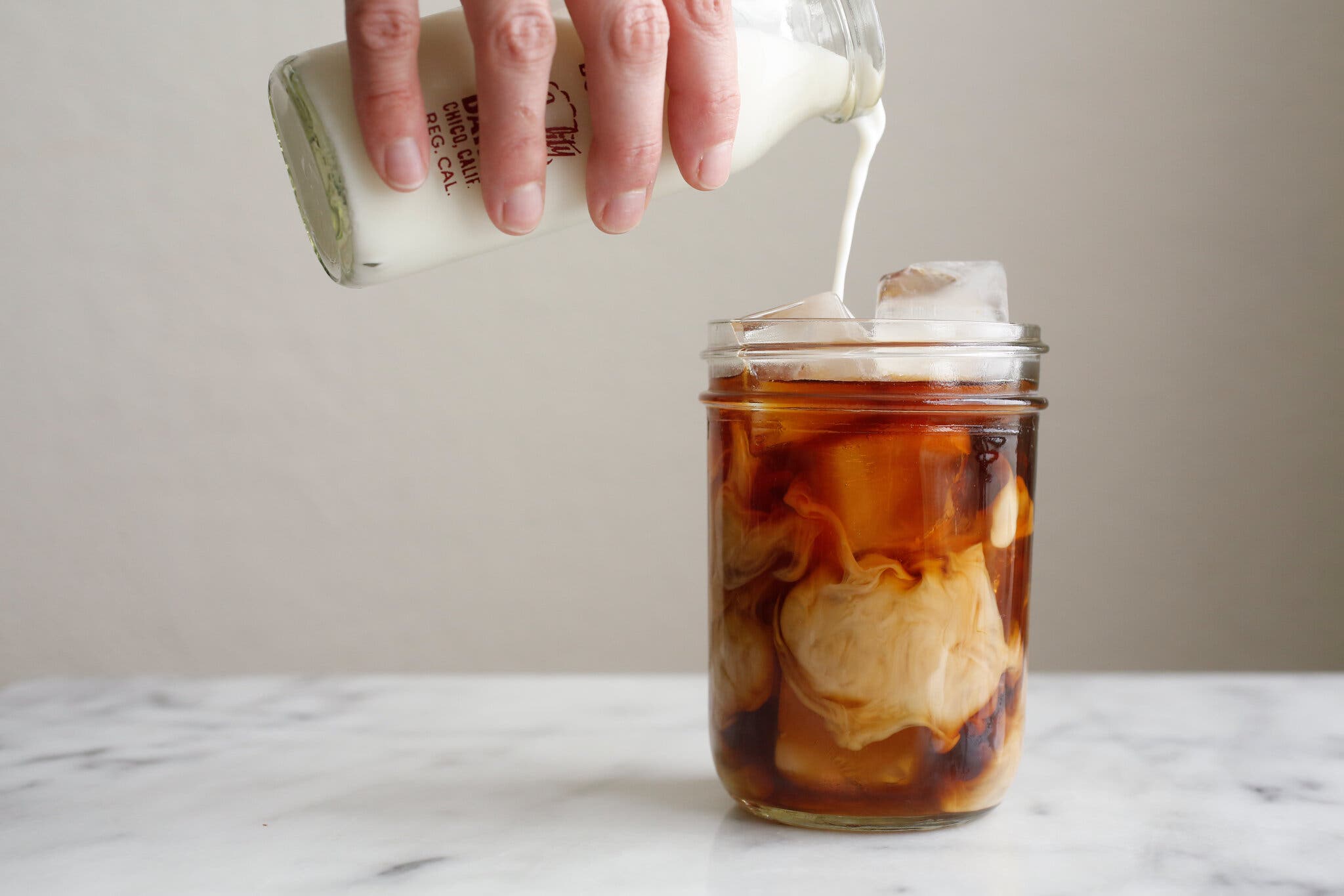 A side image of an iced coffee being topped off with milk.