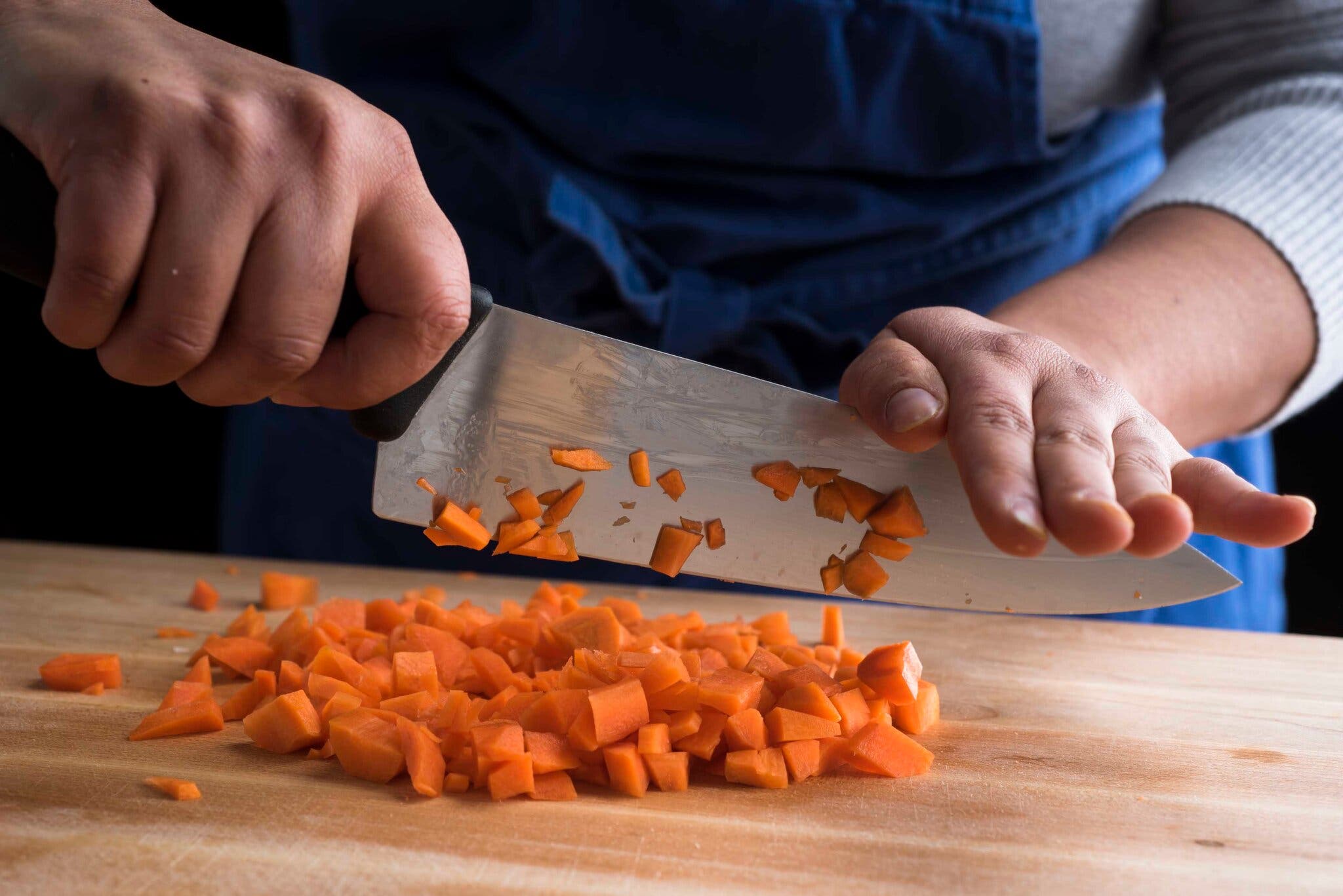 A side image of a cook cutting a carrot with a chef’s knife.