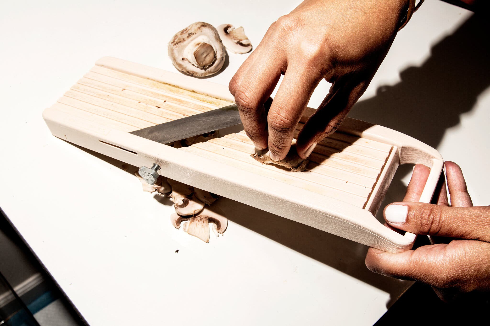 An overhead image of a hand slicing a mushroom on a mandoline.