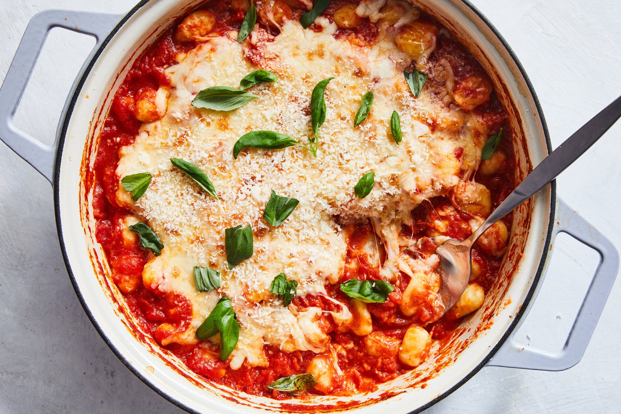 An overhead image of a pot of cheesy baked gnocchi with spicy tomato sauce, topped with Parmesan and basil.