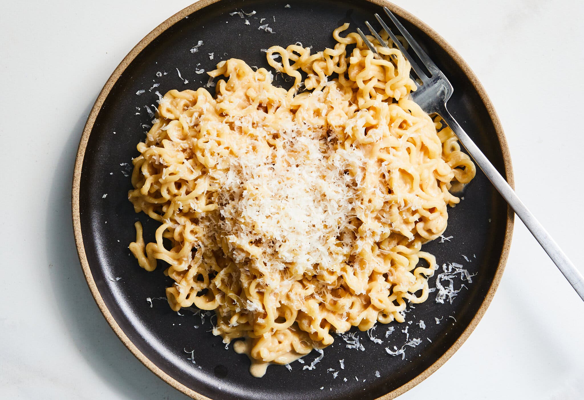 An overhead image of a black plate with peanut butter ramen noodles topped with Parmesan.