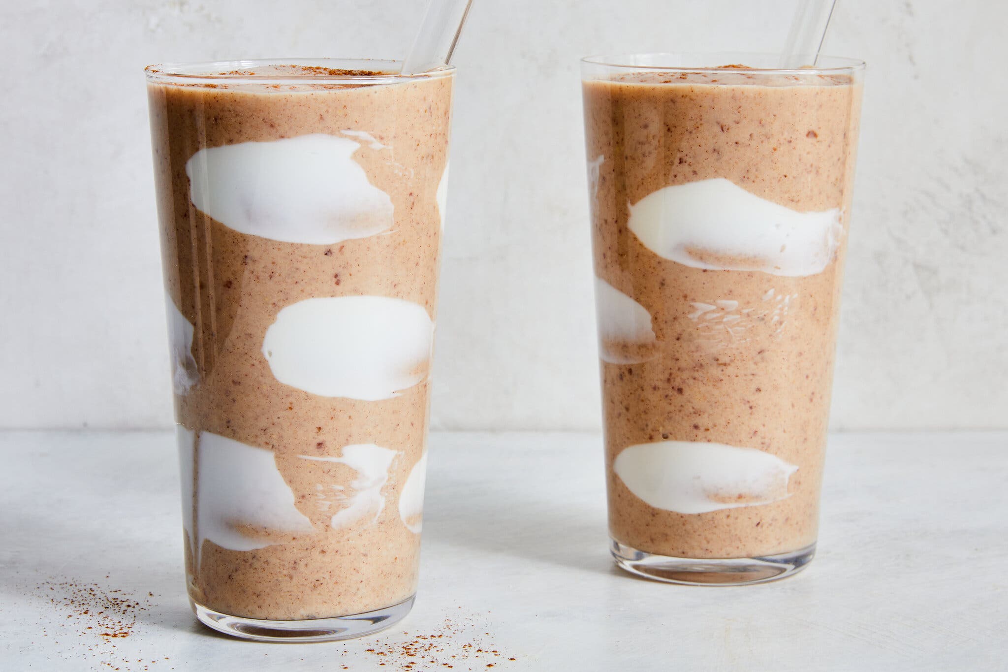 Two glasses of cinnamon date smoothie with glass straws.