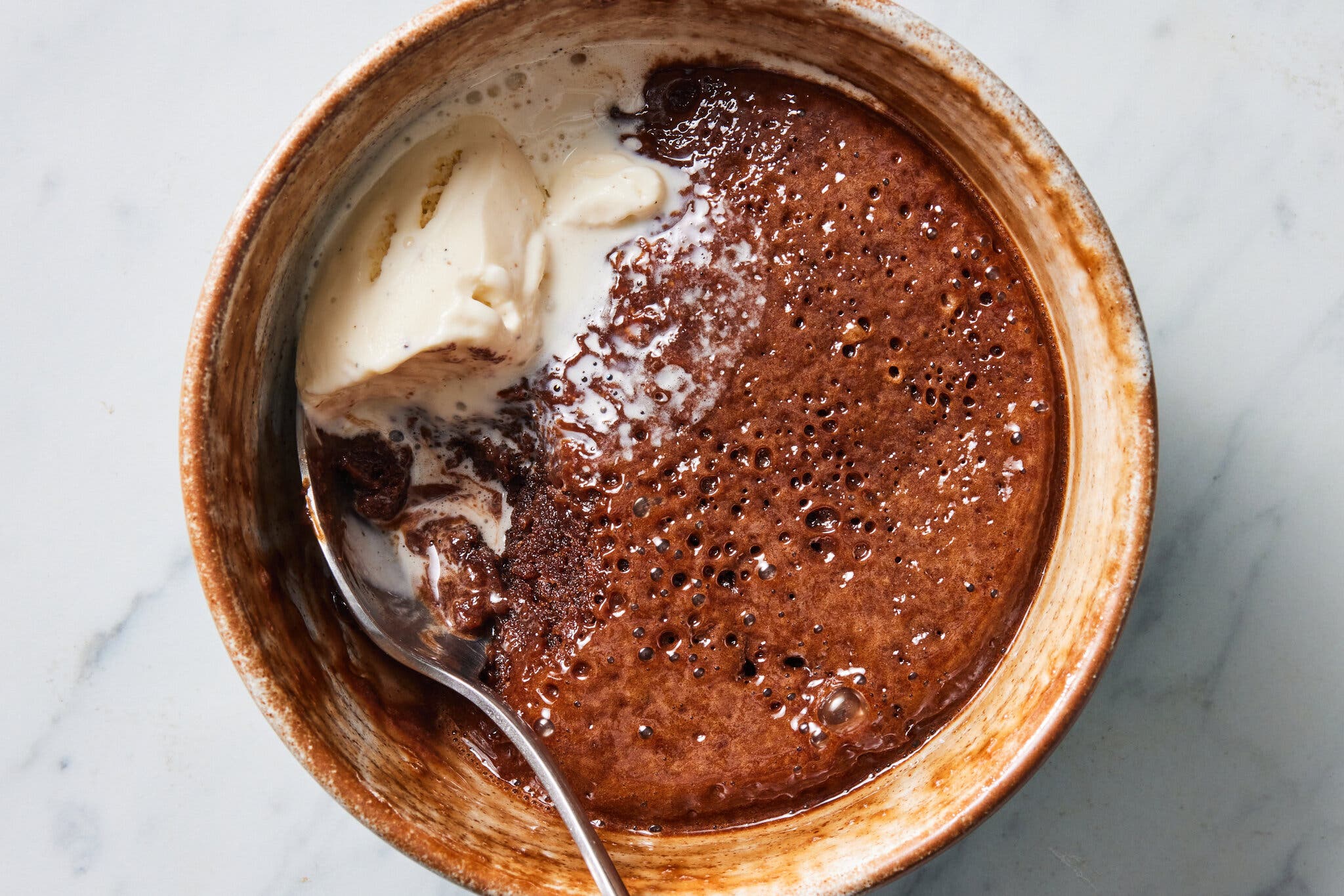 An overhead image of a small bowl of microwave Nutella pudding cake with a spoon of ice cream on top.