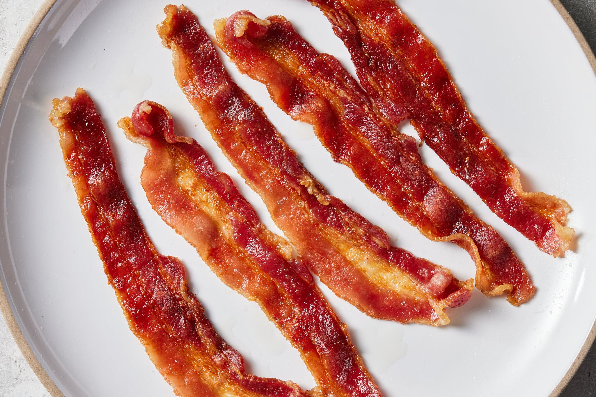 An overhead image of a plate with five strips of cooked bacon.