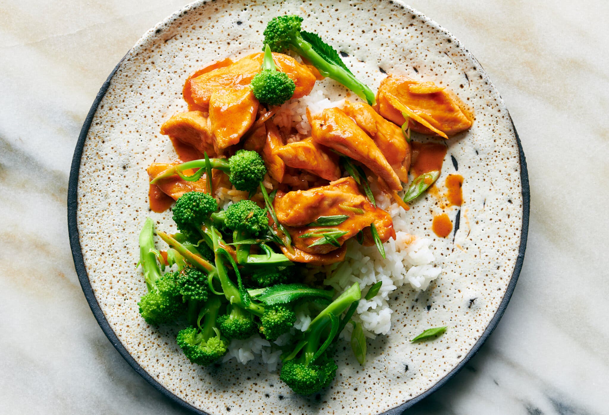 An overhead image of a plate of coconut-Gochujang glazed chicken with a side or white rice and broccoli.