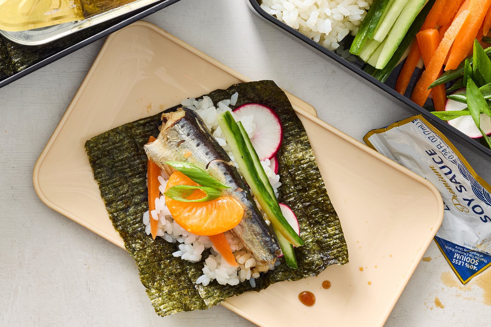 An overhead image of several food containers holding nori, rice, carrots, scallions and more.