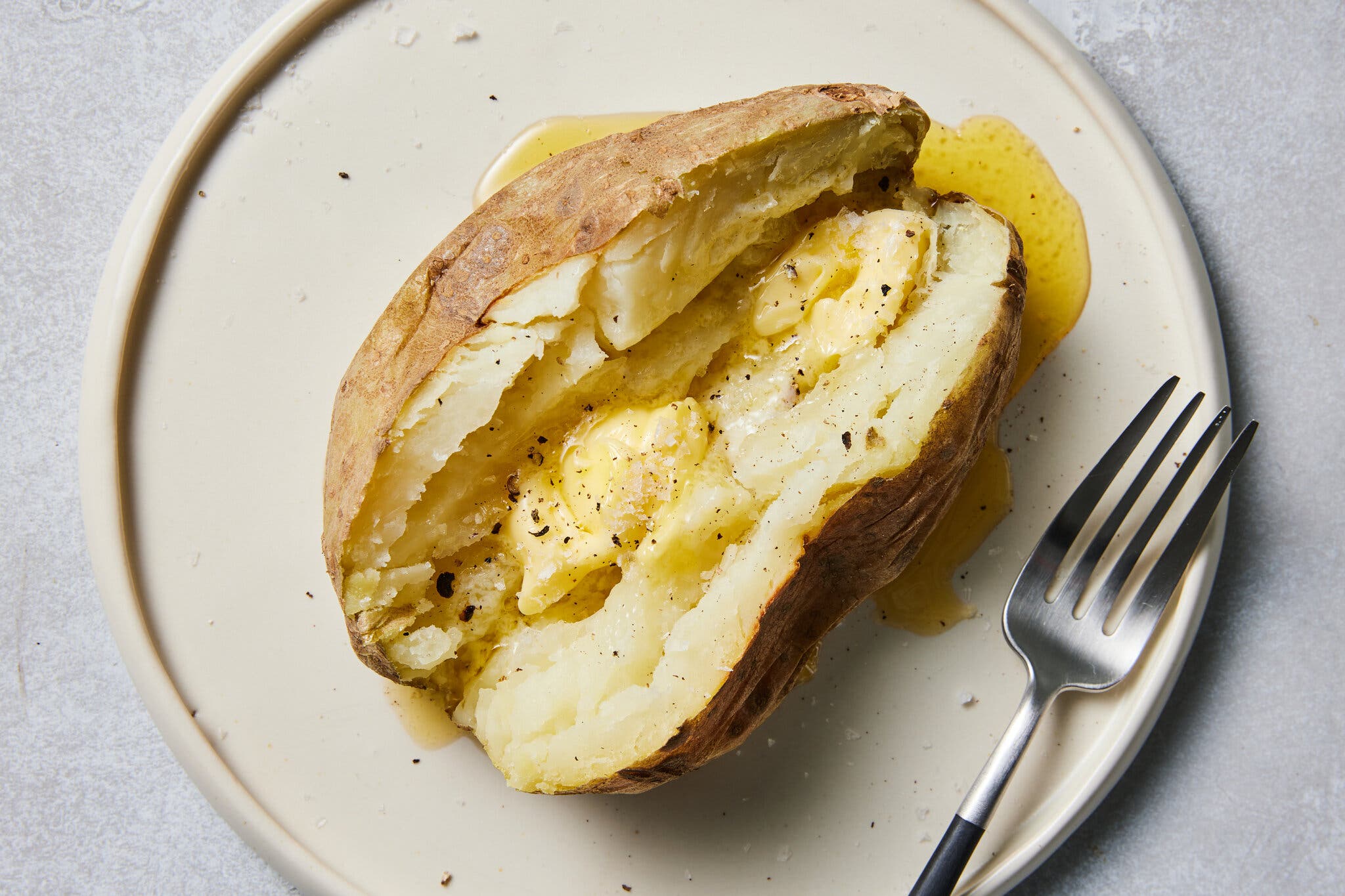 An overhead image of a baked potato sliced down the middle with butter inside and pooling at the edge.