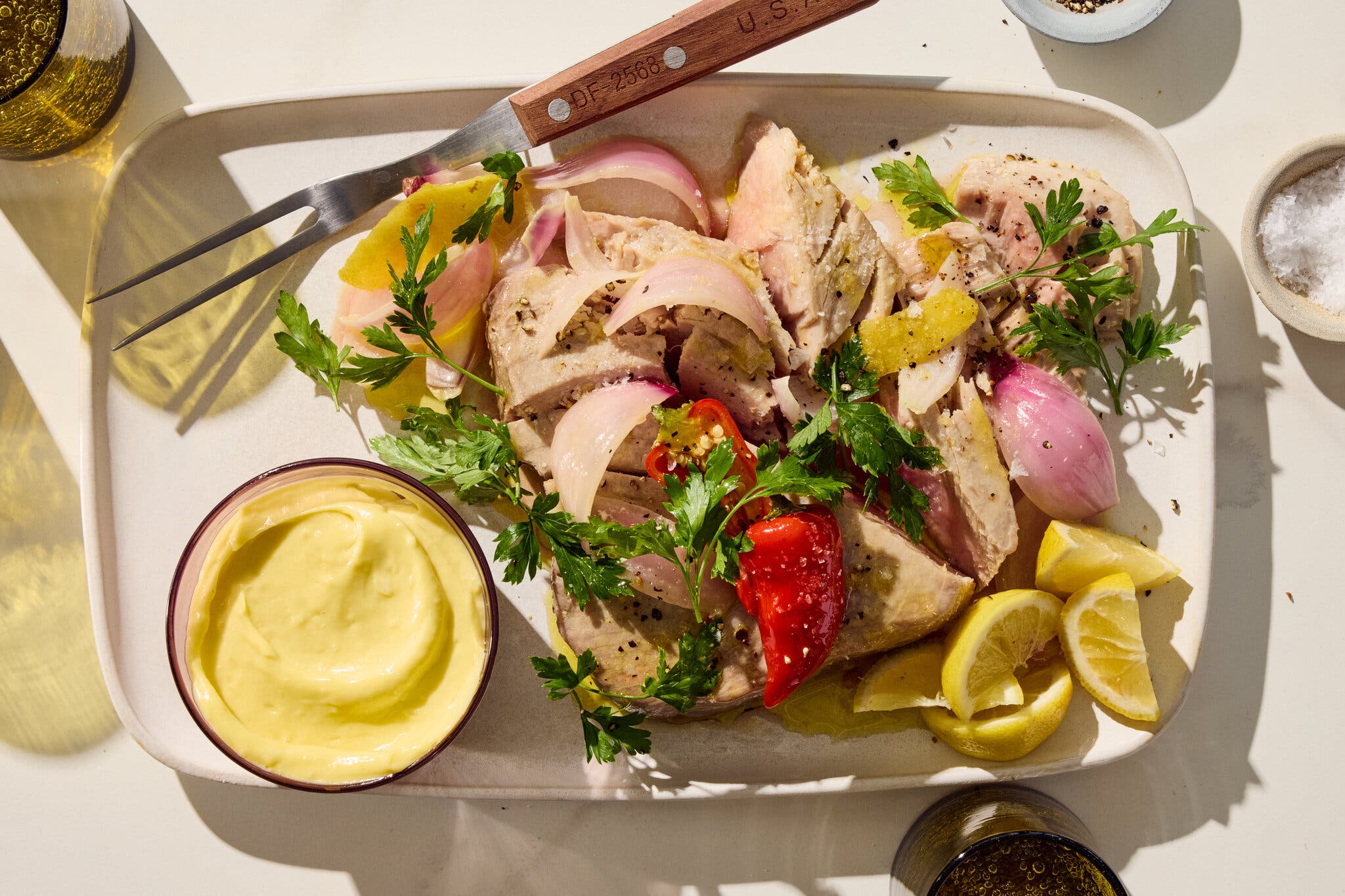 An overhead image of tuna topped with shallots next to an aioli and spent lemon wedges.