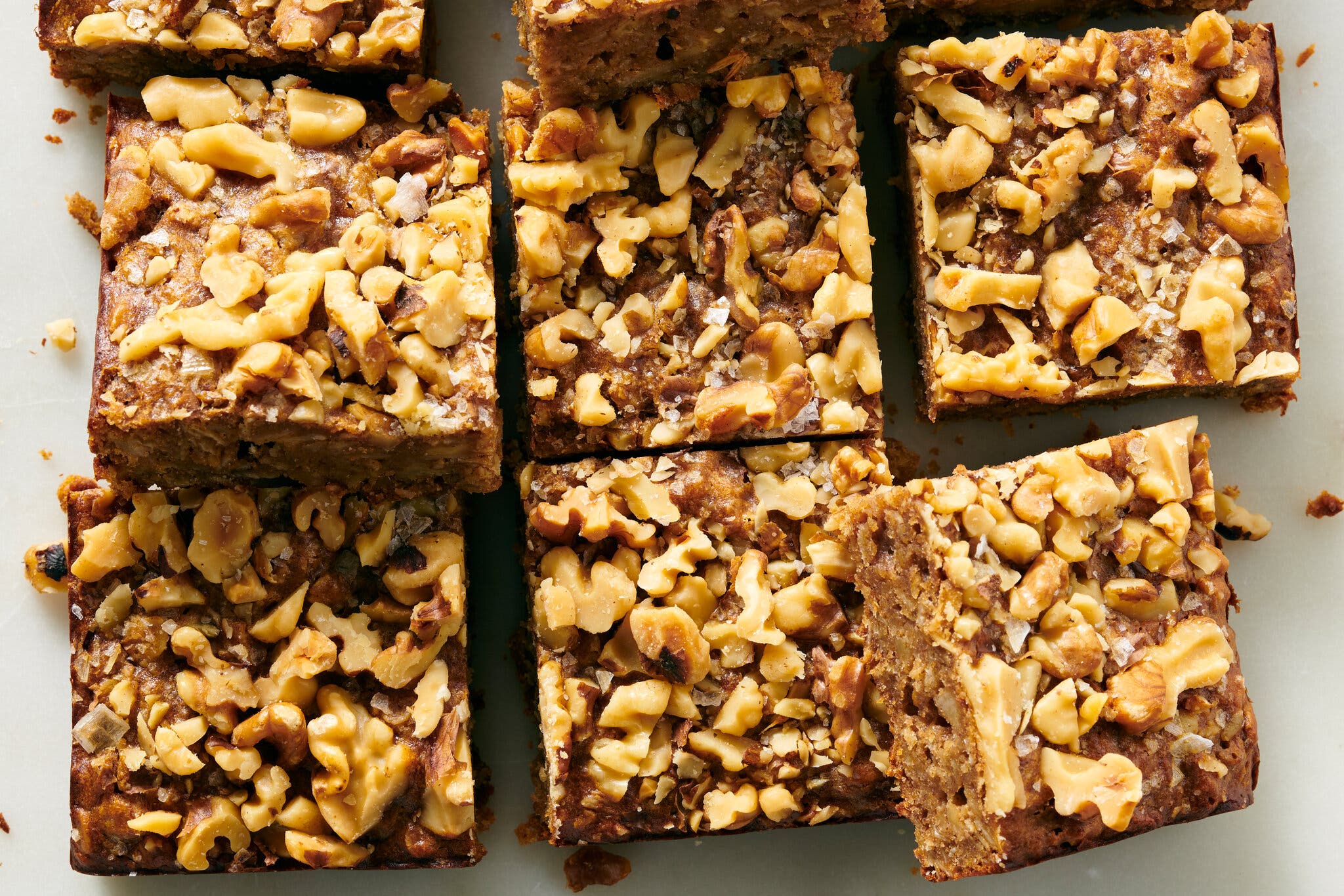 Nine breakfast bars topped with nuts are photographed from overhead on a white surface.