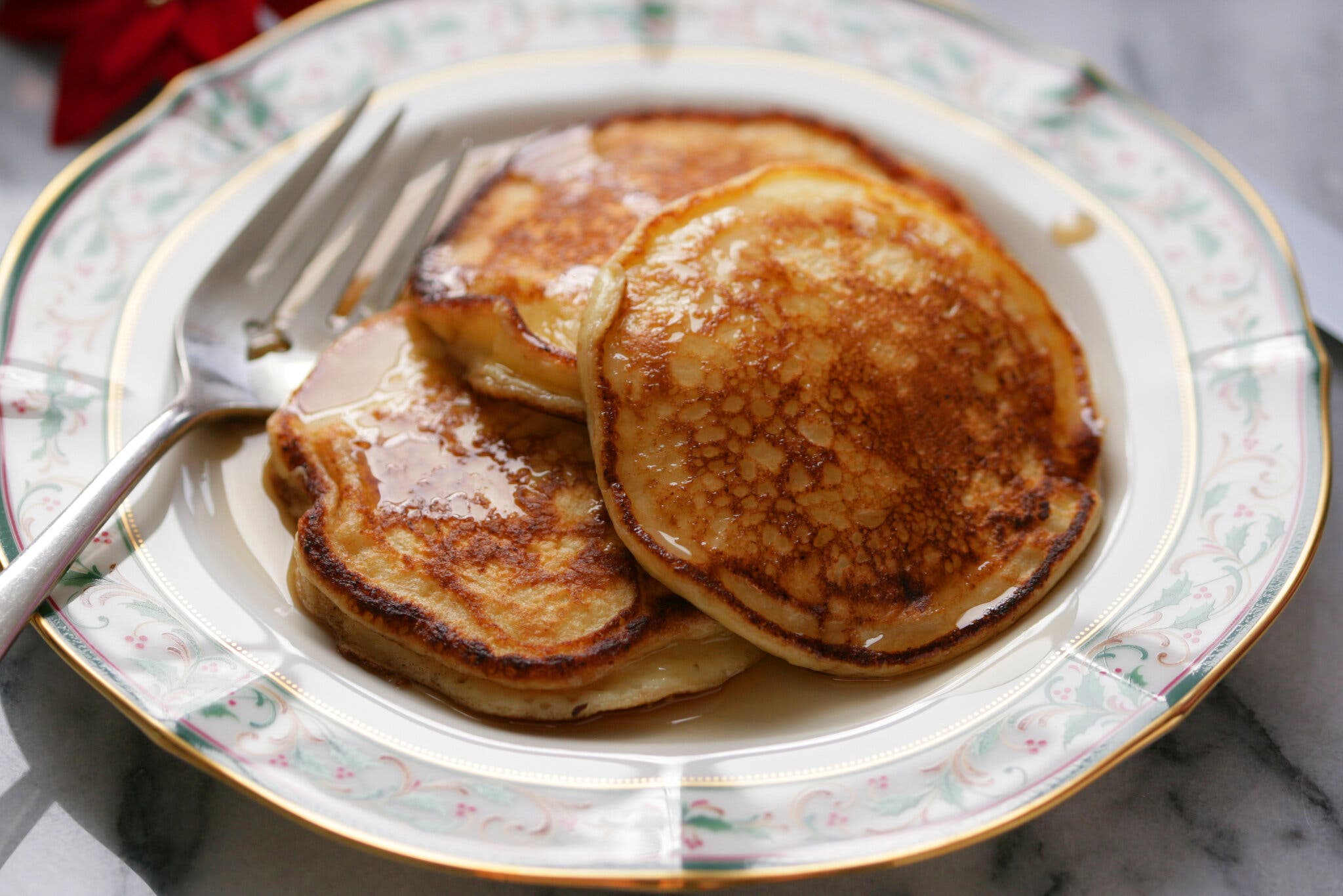 A small stack of pancakes glossed with syrup is photographed at an angle.