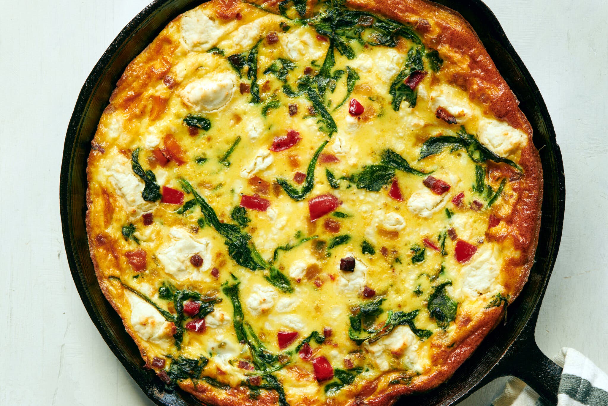 A frittata filled with cheese and vegetables is baked into a cast-iron skillet.