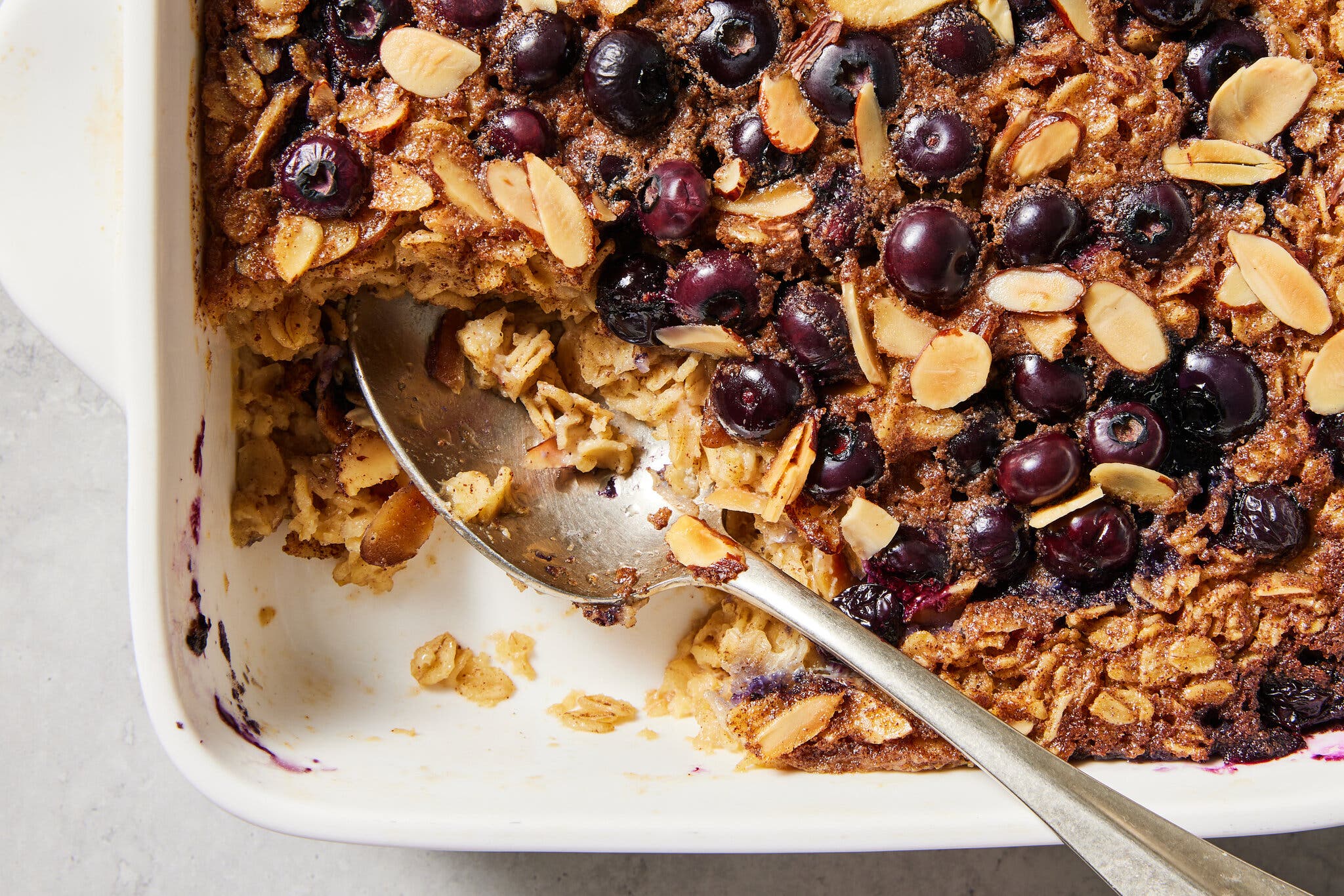 A baking dish full of baked oatmeal studded with nuts and blueberries is photographed from overhead.
