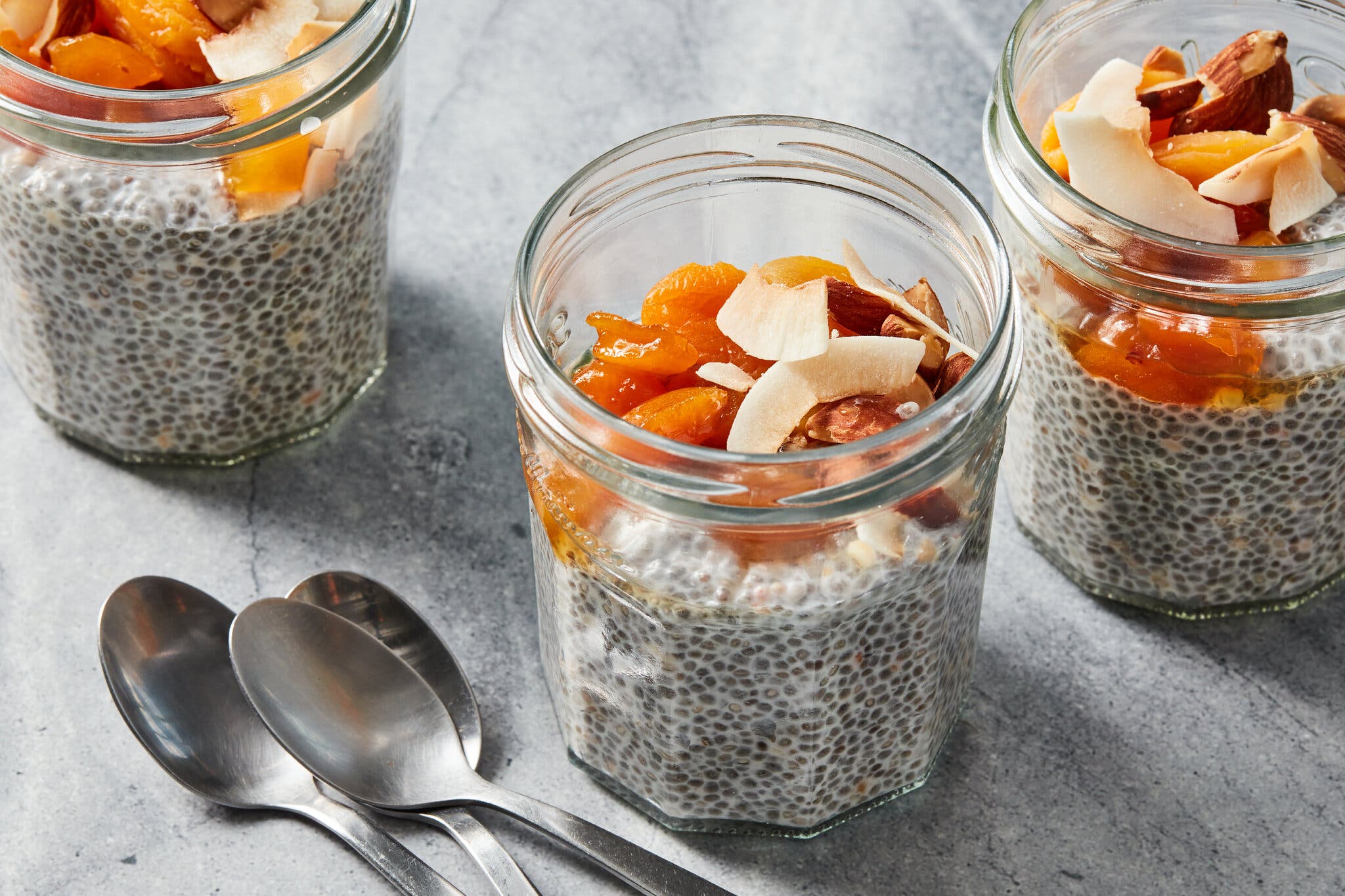 Three jars filled with chia seed pudding and topped with fruits and nuts are photographed at an angle.