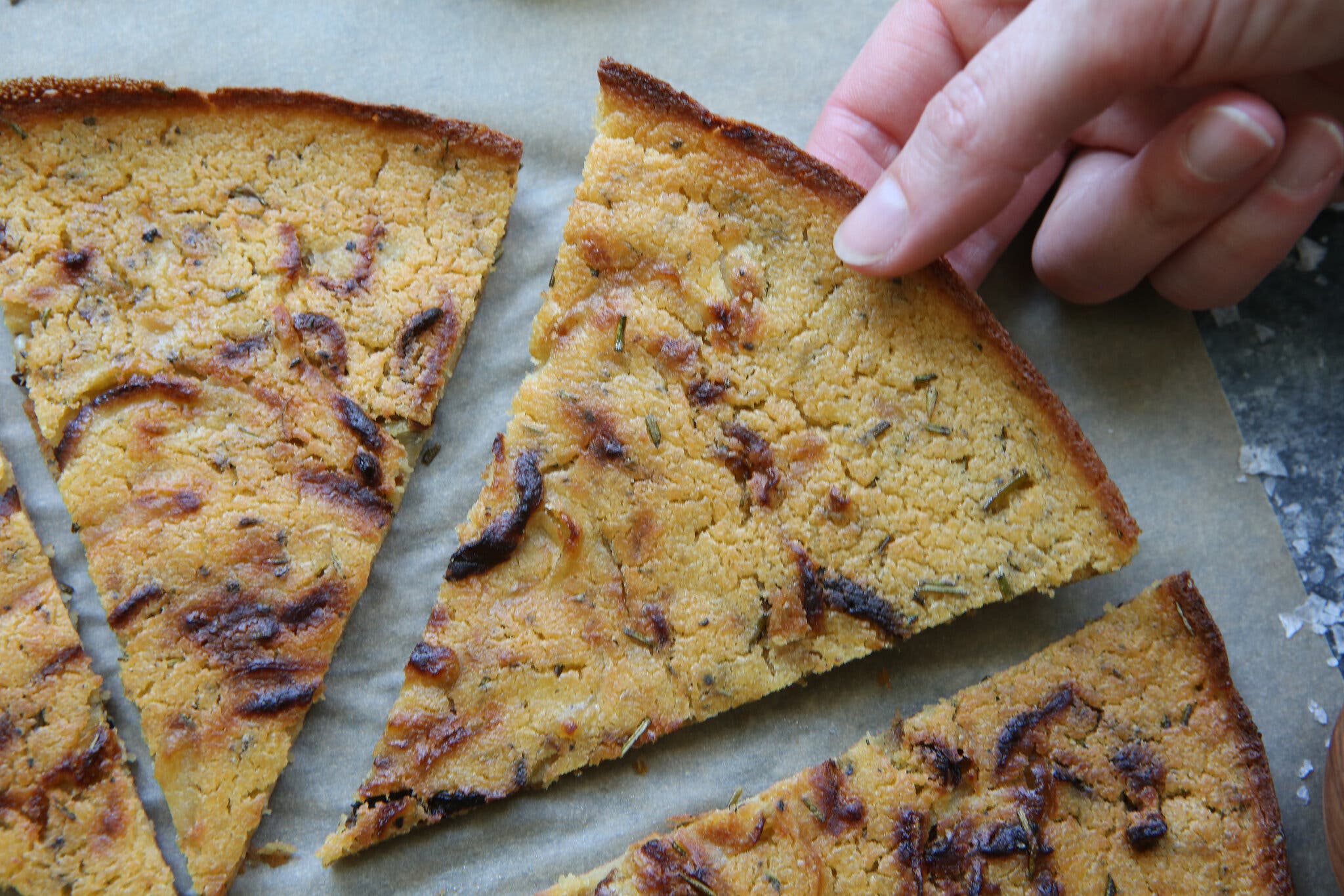 A crisp chickpea pancake studded with herbs is photographed from overhead.