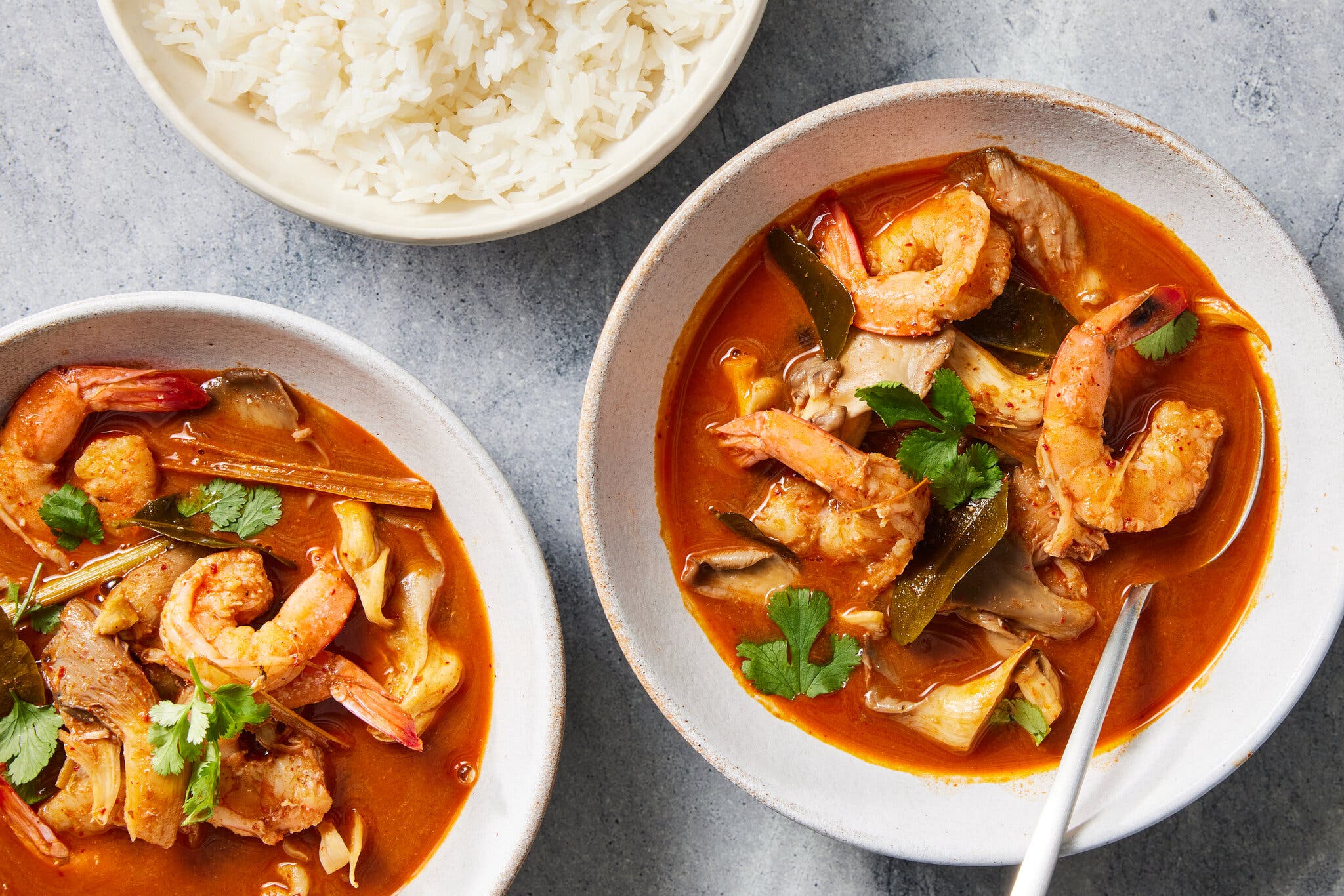 Two bowls of tom yum goong soup, a Thai hot and sour shrimp soup, with a bowl of white rice alongside.