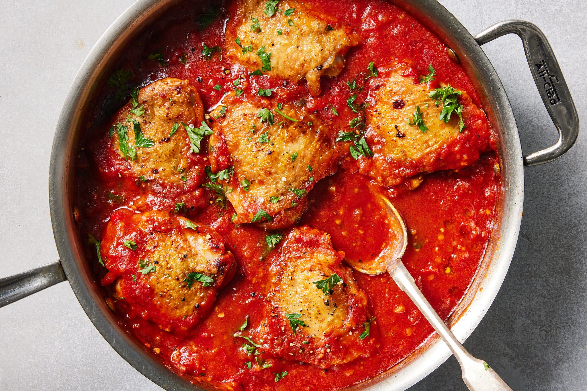 A large skillet with golden brown chicken thighs, nestled in a spicy tomato sauce.