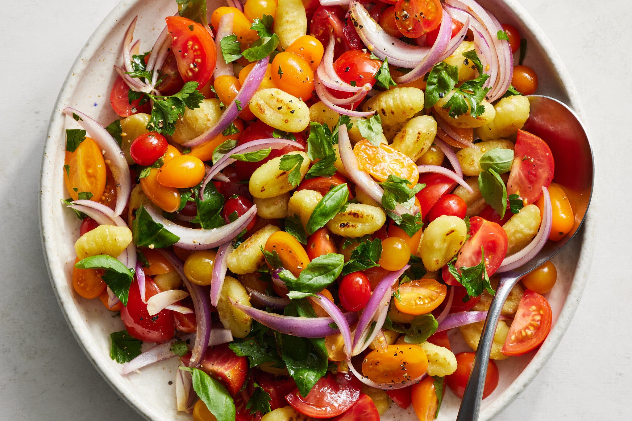 An overhead image of a pasta salad with gnocchi and tomatoes.