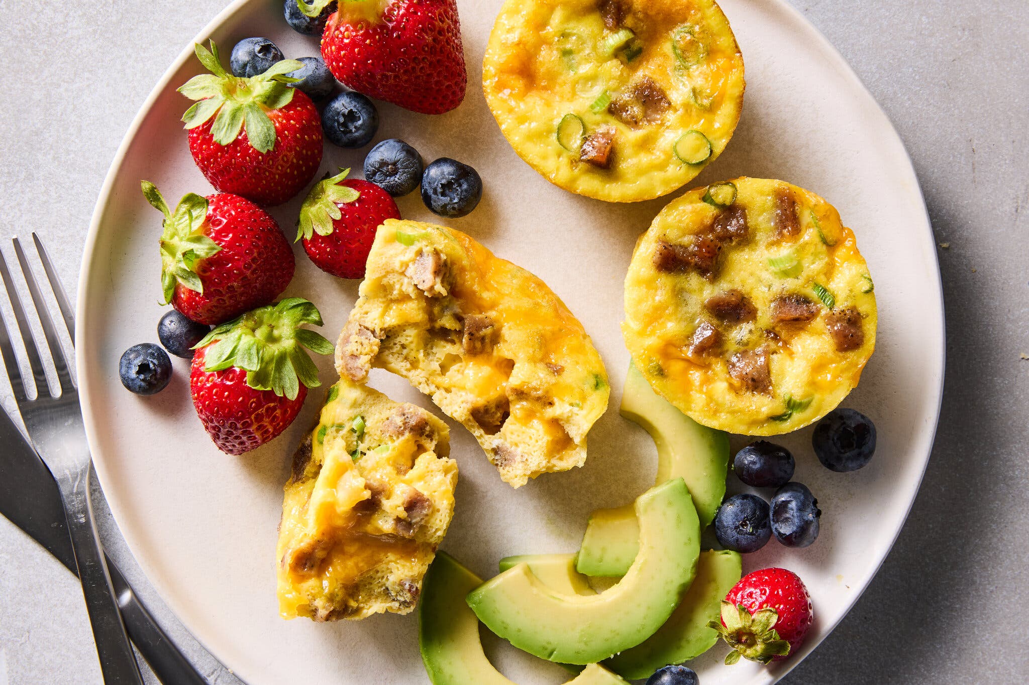 An overhead image of egg bites on a plate paired with eggs and sliced avocado.