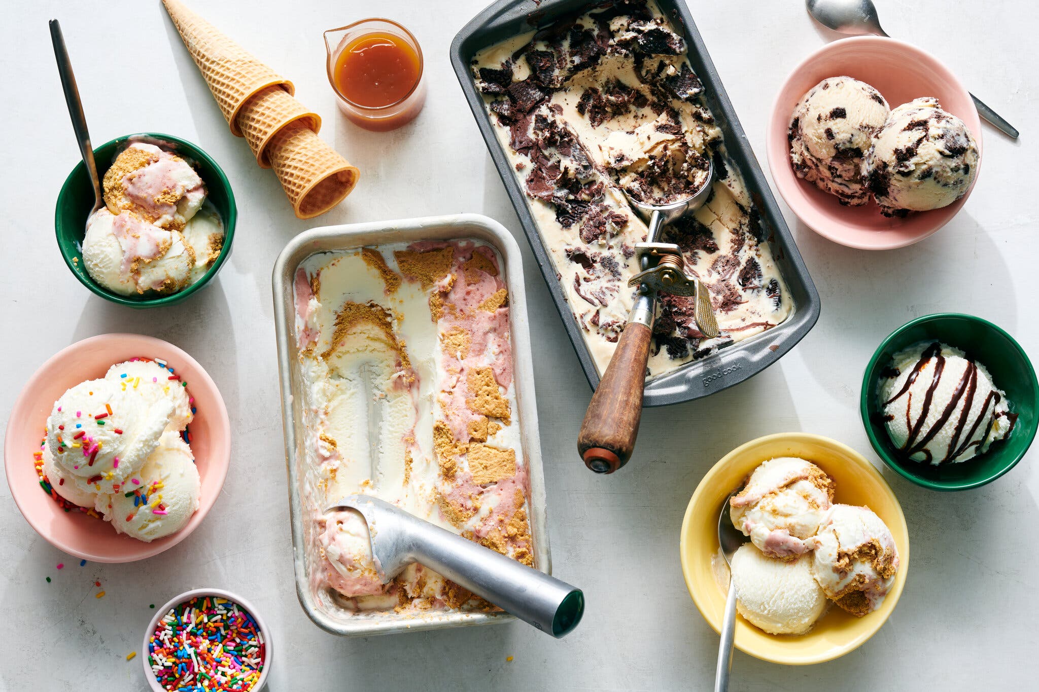 Ice cream from two metal loaf pans is scooped into small colorful bowls.