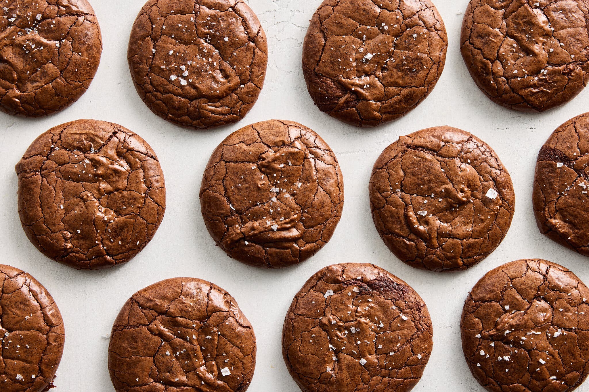 An overhead image of a dozen brownie cookies topped with flaky salt.