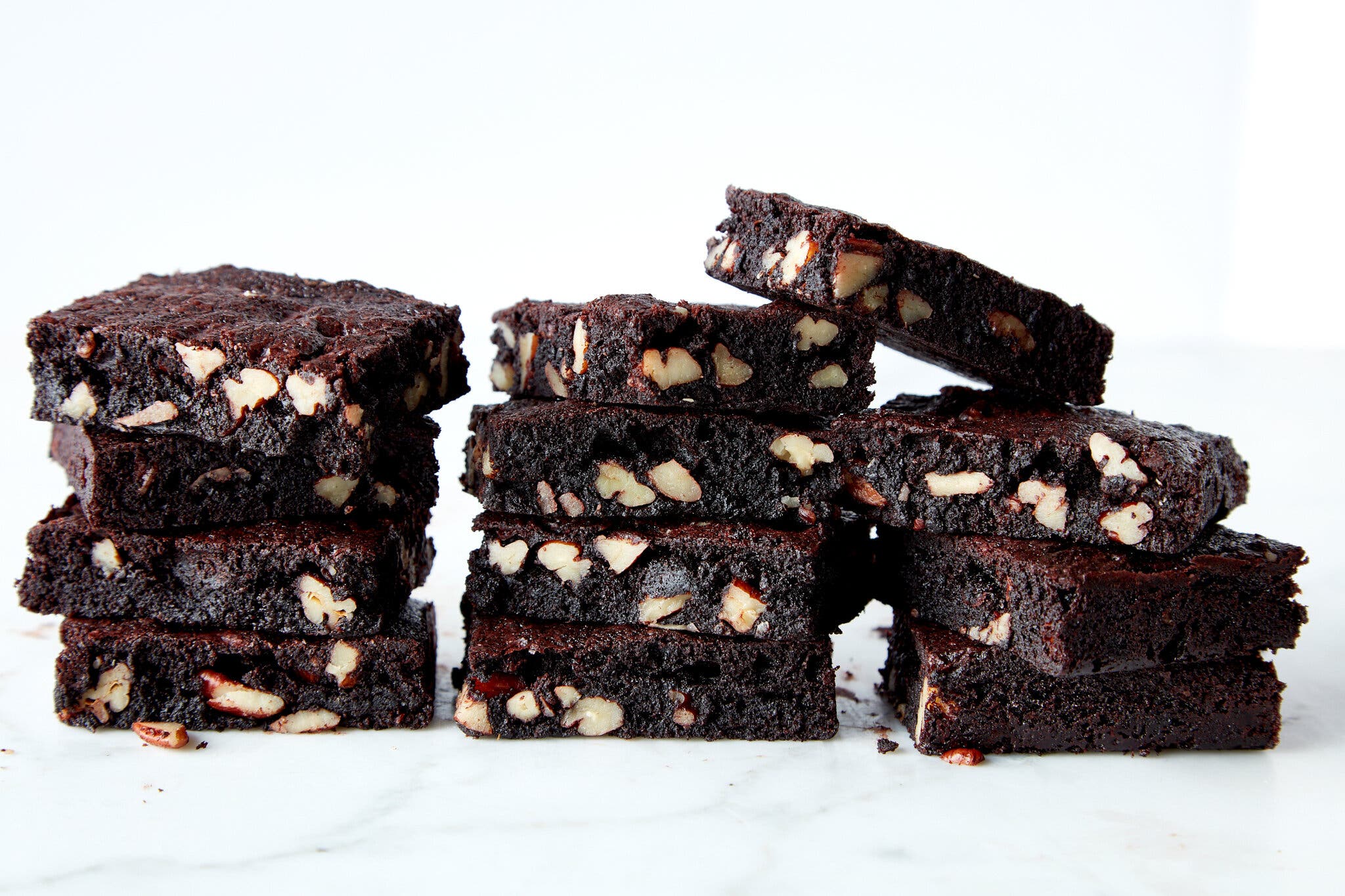 Three stacks of brownies studded with chopped walnuts on a marble counter.