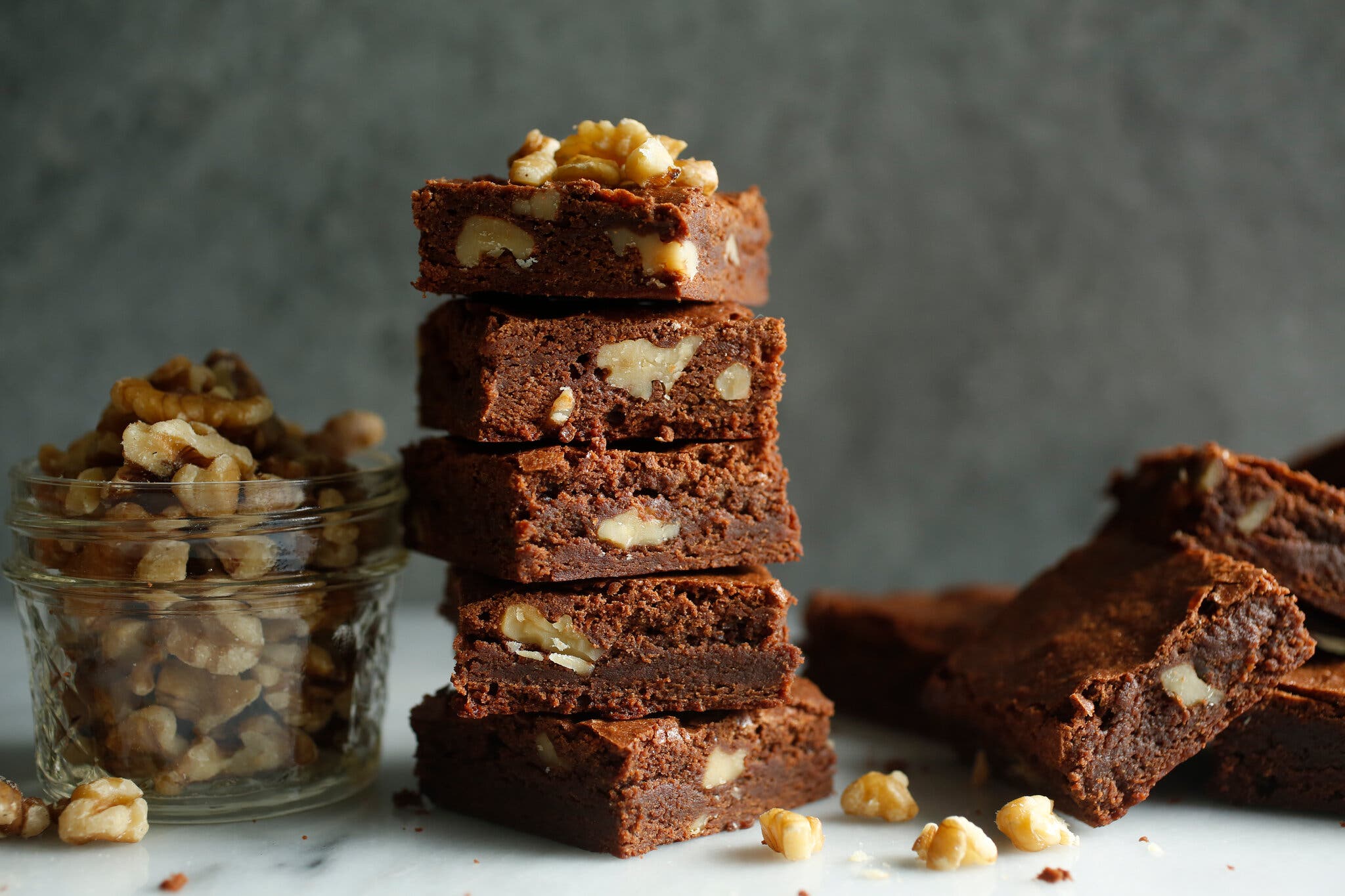 A stack of five brownies with walnuts. To the left, a small Mason jar with more chopped walnuts.