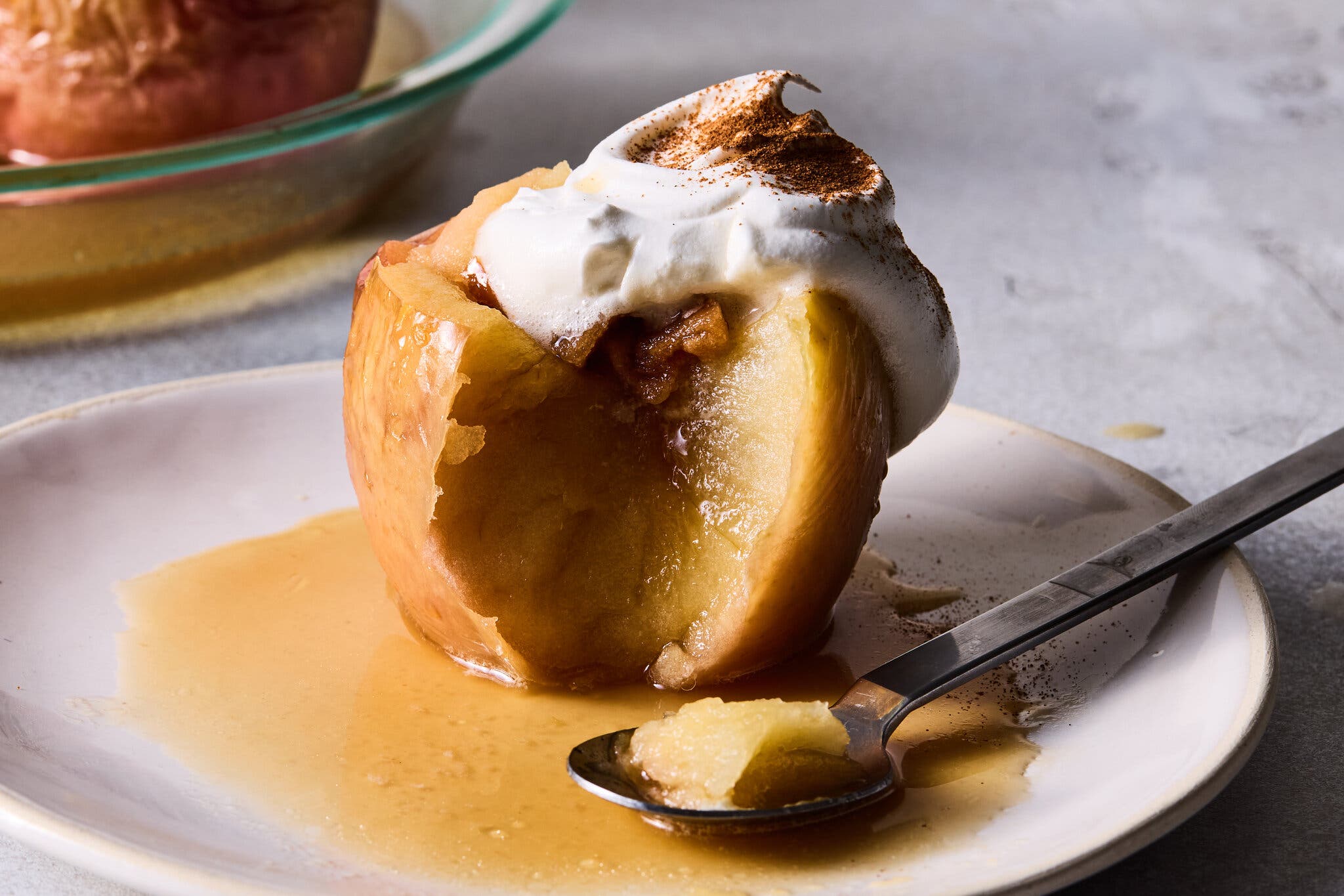 A stuffed baked apple with a piece broken off is topped with whipped cream and cinnamon.