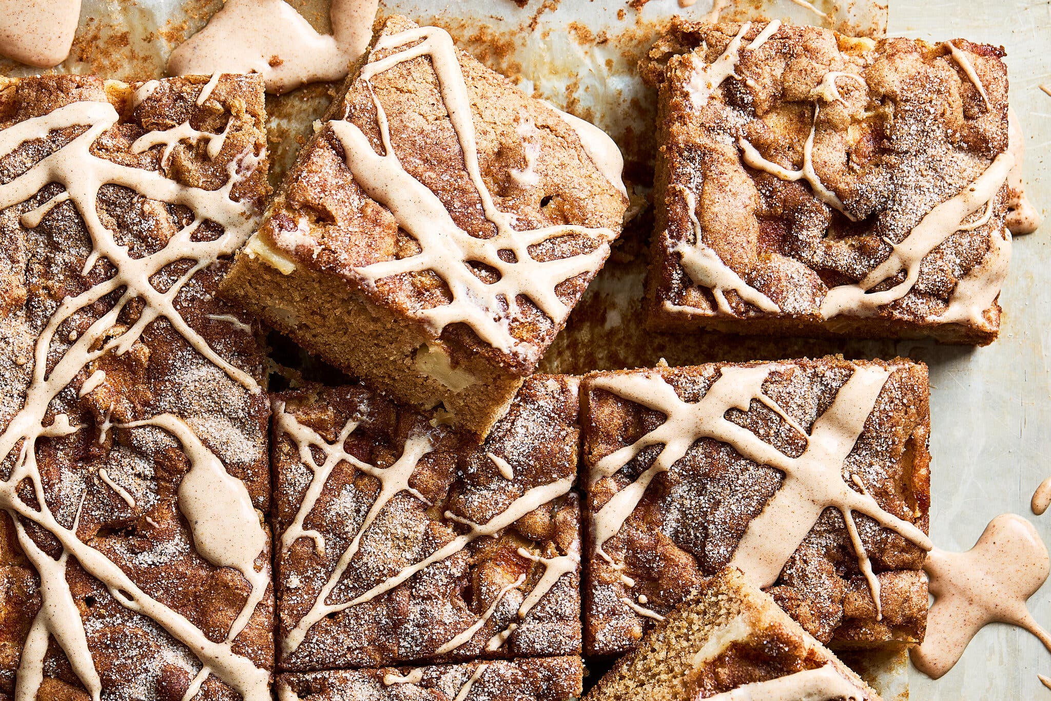 An overhead image of a cinnamon sugar dusted cake cut into squares and finished with an icing drizzle.