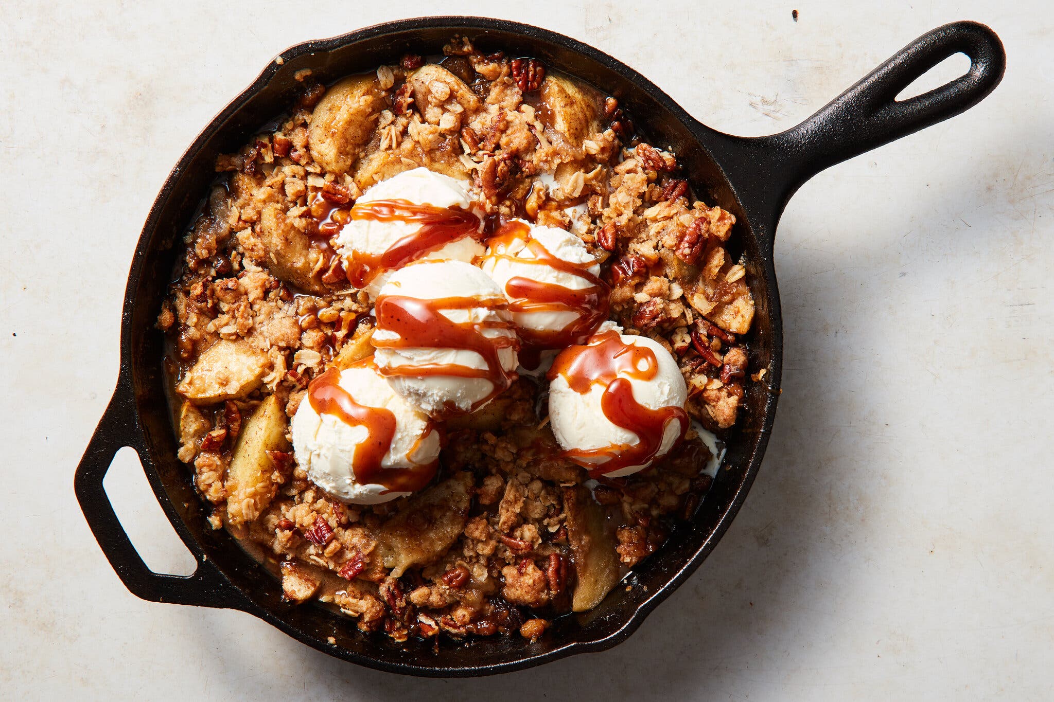 An overhead image of an apple crisp in a cast-iron skillet topped with scoops of ice cream.