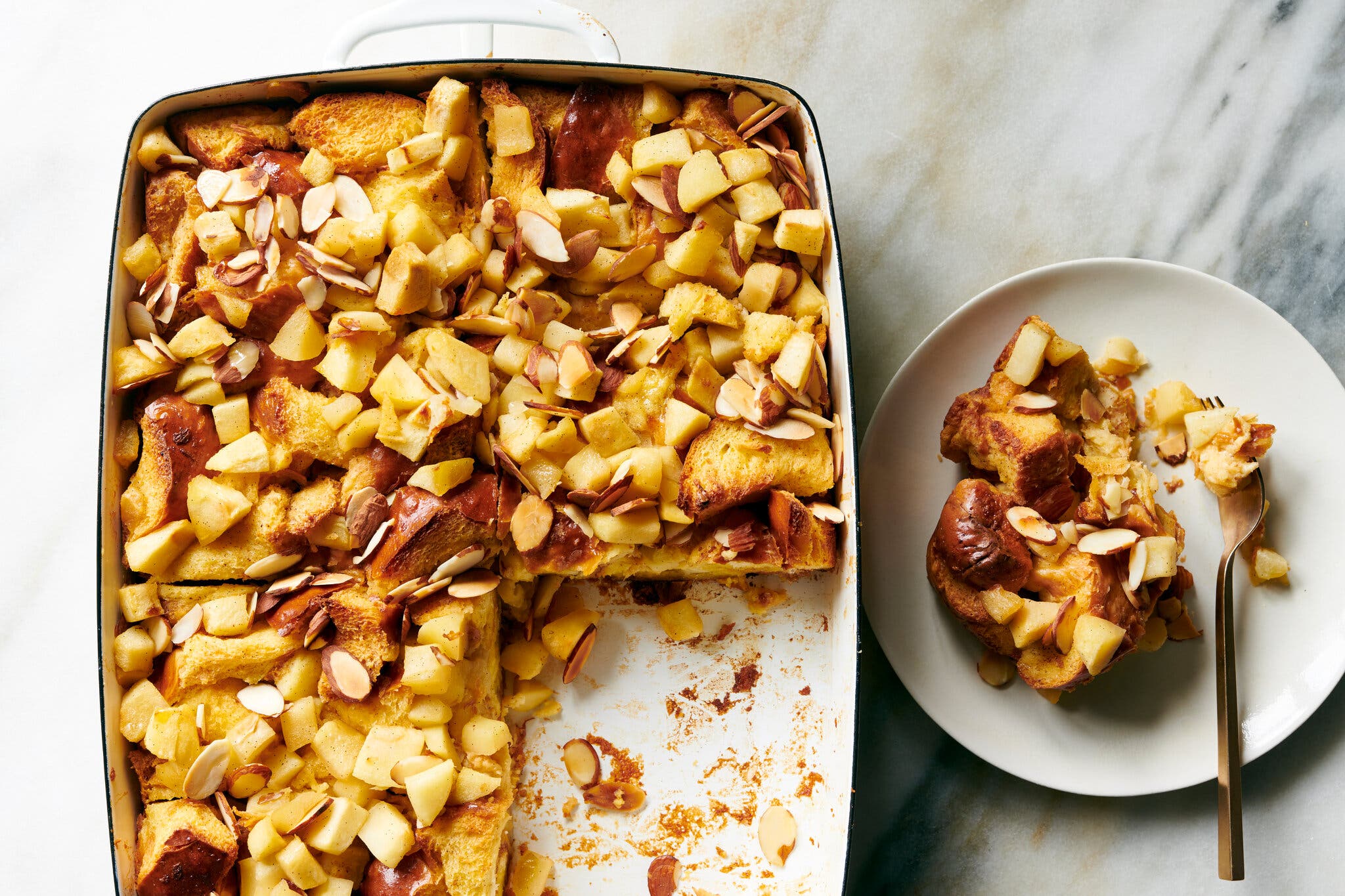 An overhead image of a baking pan filled with a bread pudding finished with chunks of apples and sliced almonds.