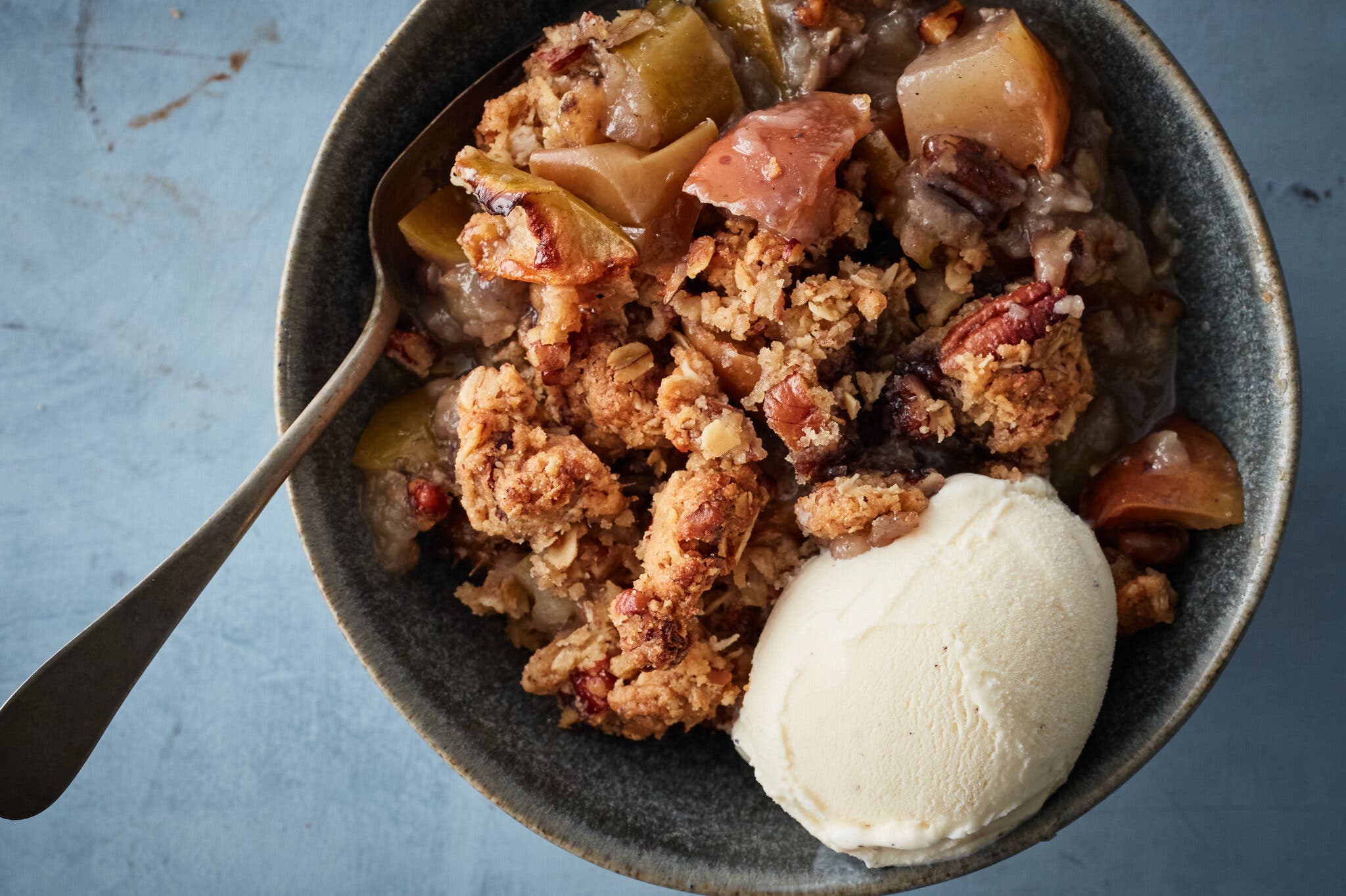An overhead image of a bowl filled with apple crisp and topped with a scoop of ice cream.