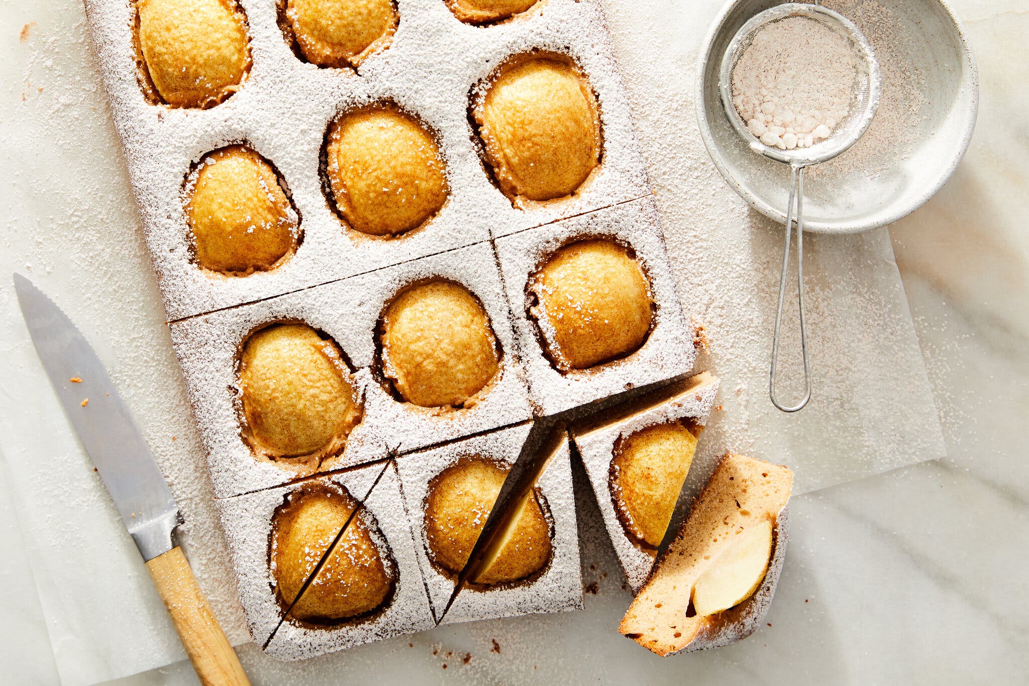 An overhead image of an apple cake dusted with powdered sugar on a sheet of parchment.