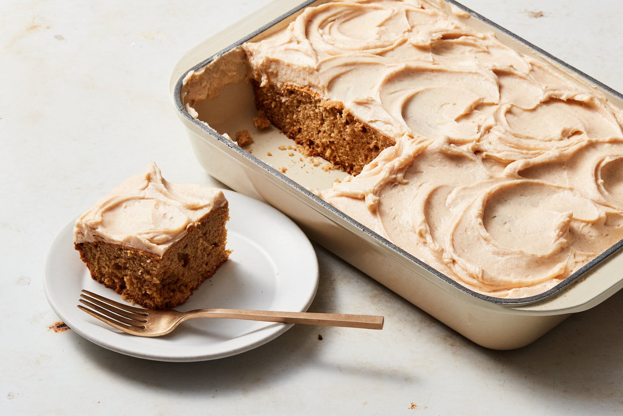 A frosted apple cake in a baking dish is shot at an angle. A couple of slices have been taken out, and one sits off to the side.