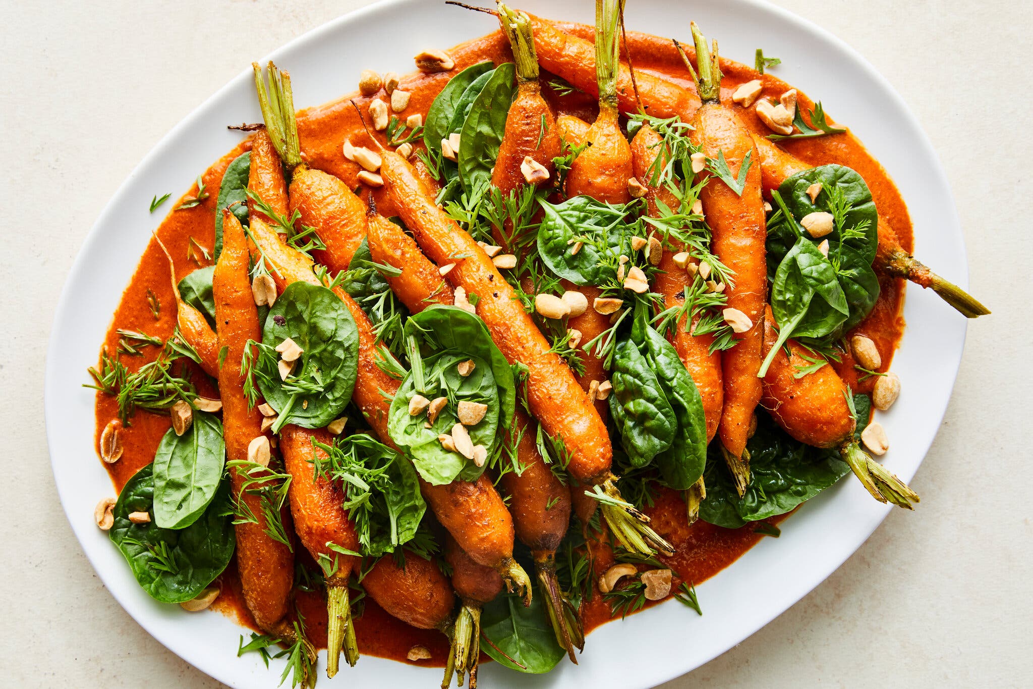 An oval white platter is filled with carrots set over sauce.