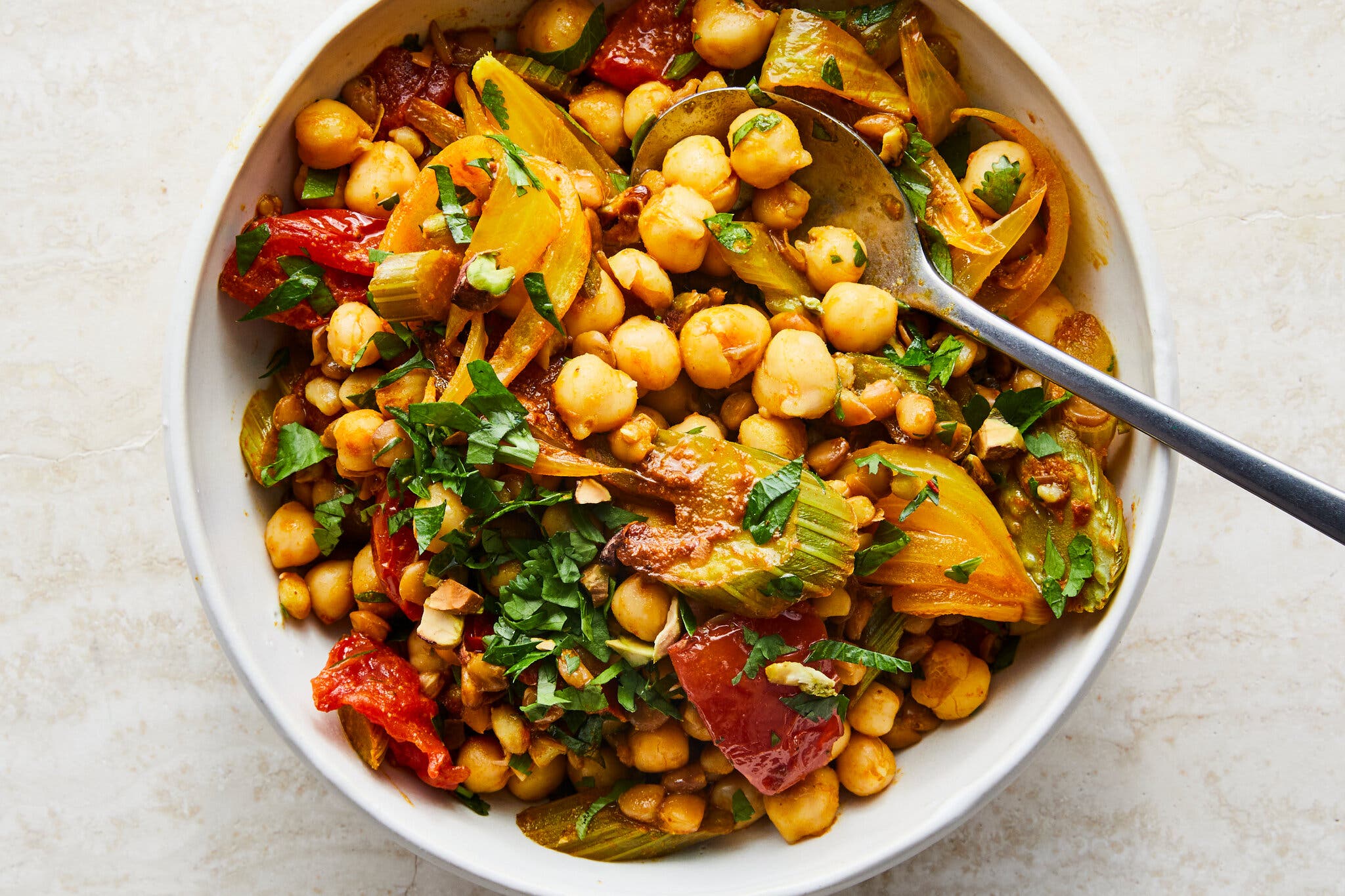 A white bowl is filled with chickpeas and roasted vegetables.
