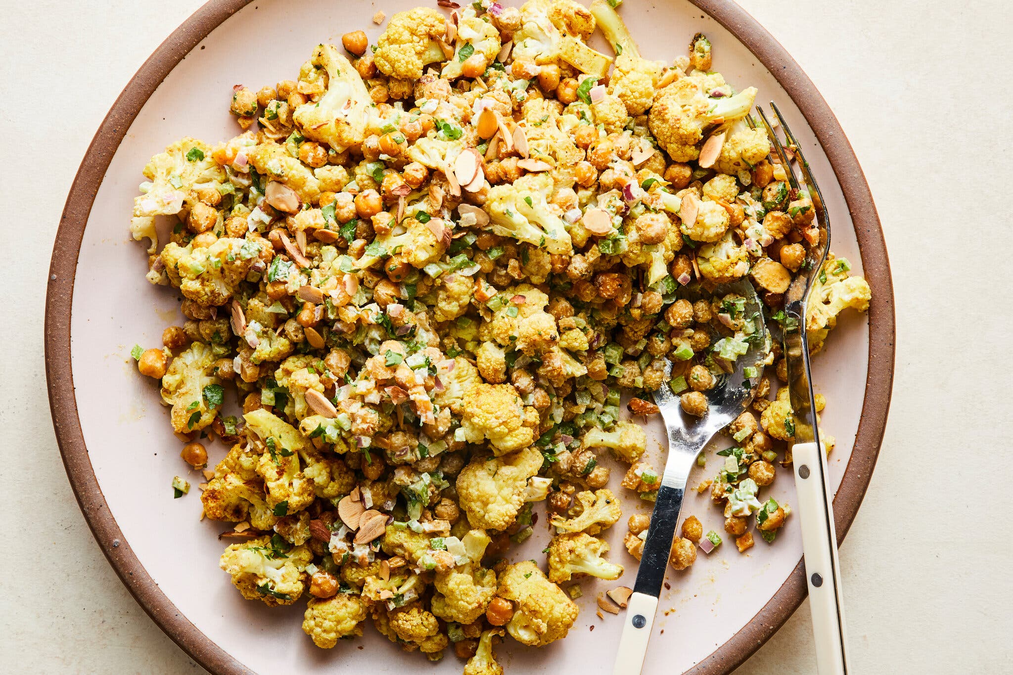 A pink plate with brown rim holds a golden cauliflower salad with chickpeas.