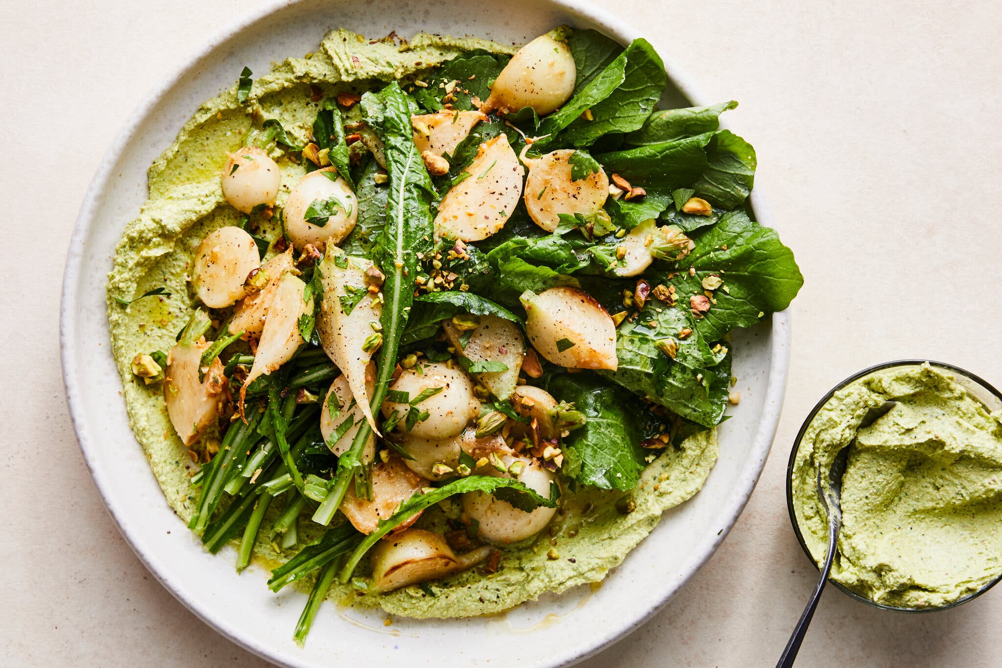 A white platter of greens and roasted turnips sit next to a bowl of creamy green dip.