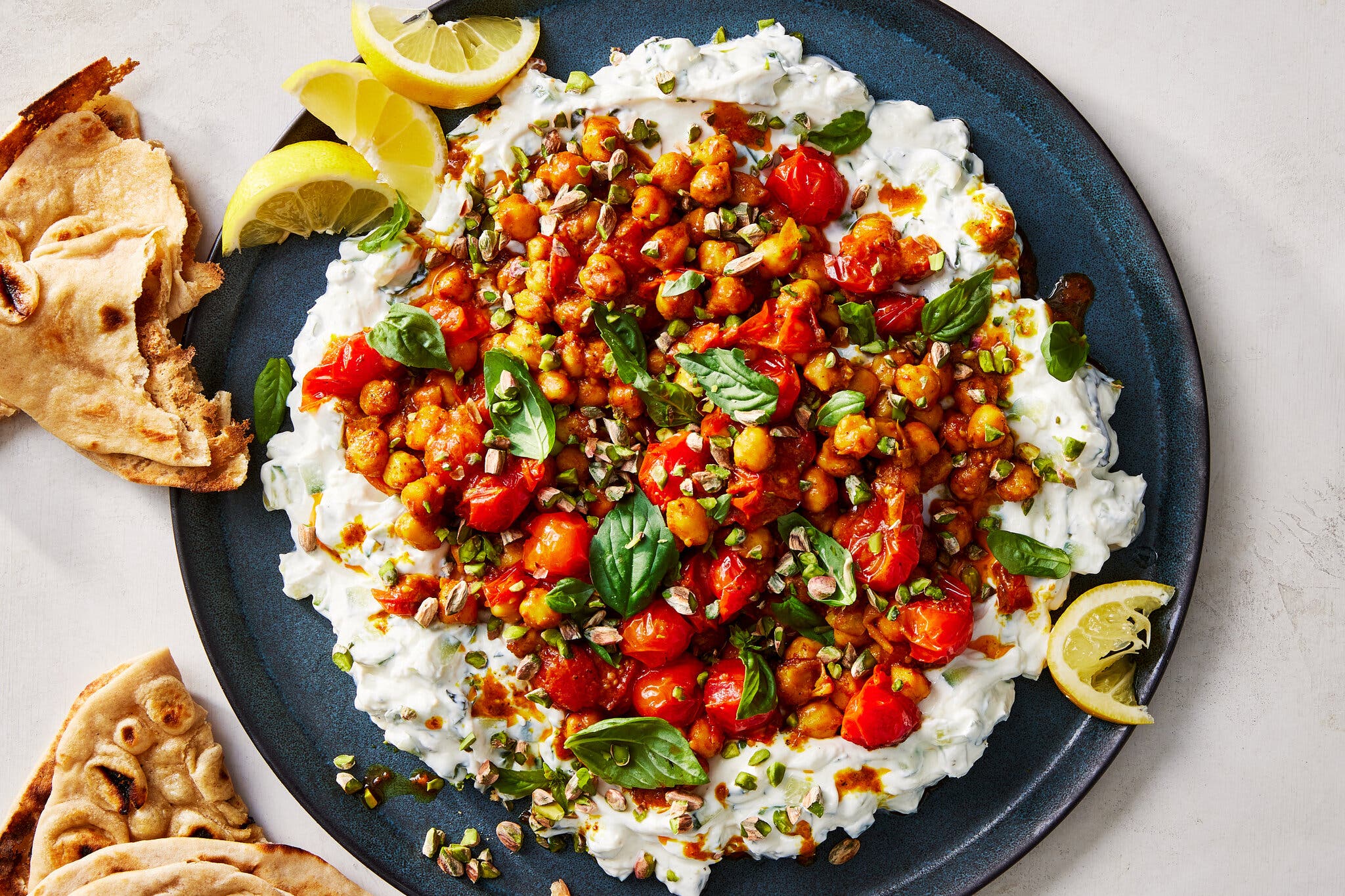 An overhead image of chickpeas and tomatoes on a bed of yogurt next to some flatbread.