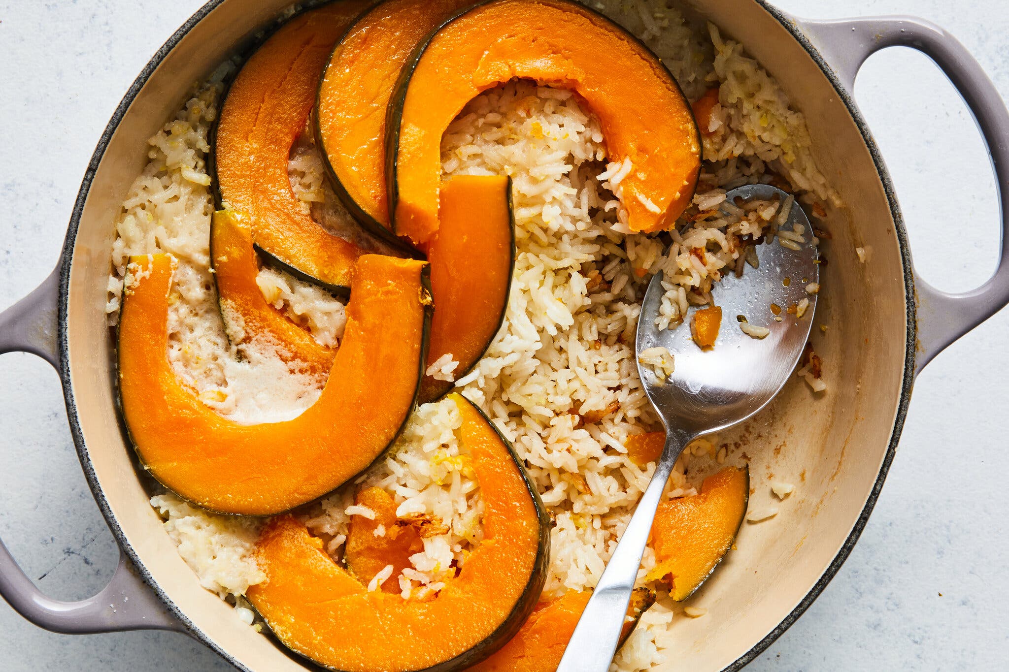 An overhead shot of a Dutch oven full of rice, with slices of kabocha squash shingled on top. There is a serving spoon in the pot.