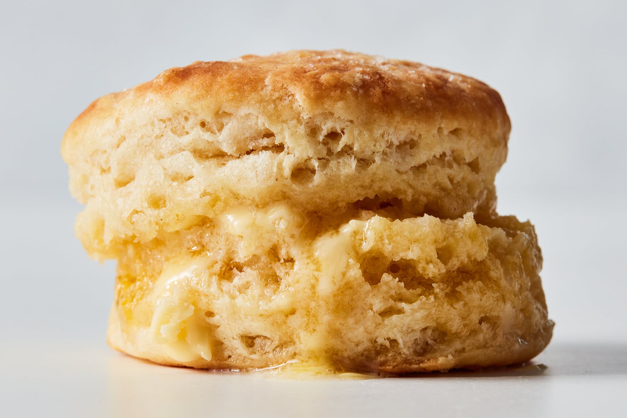 A close-up shot of a biscuit, sliced in half, with butter oozing out of the middle.