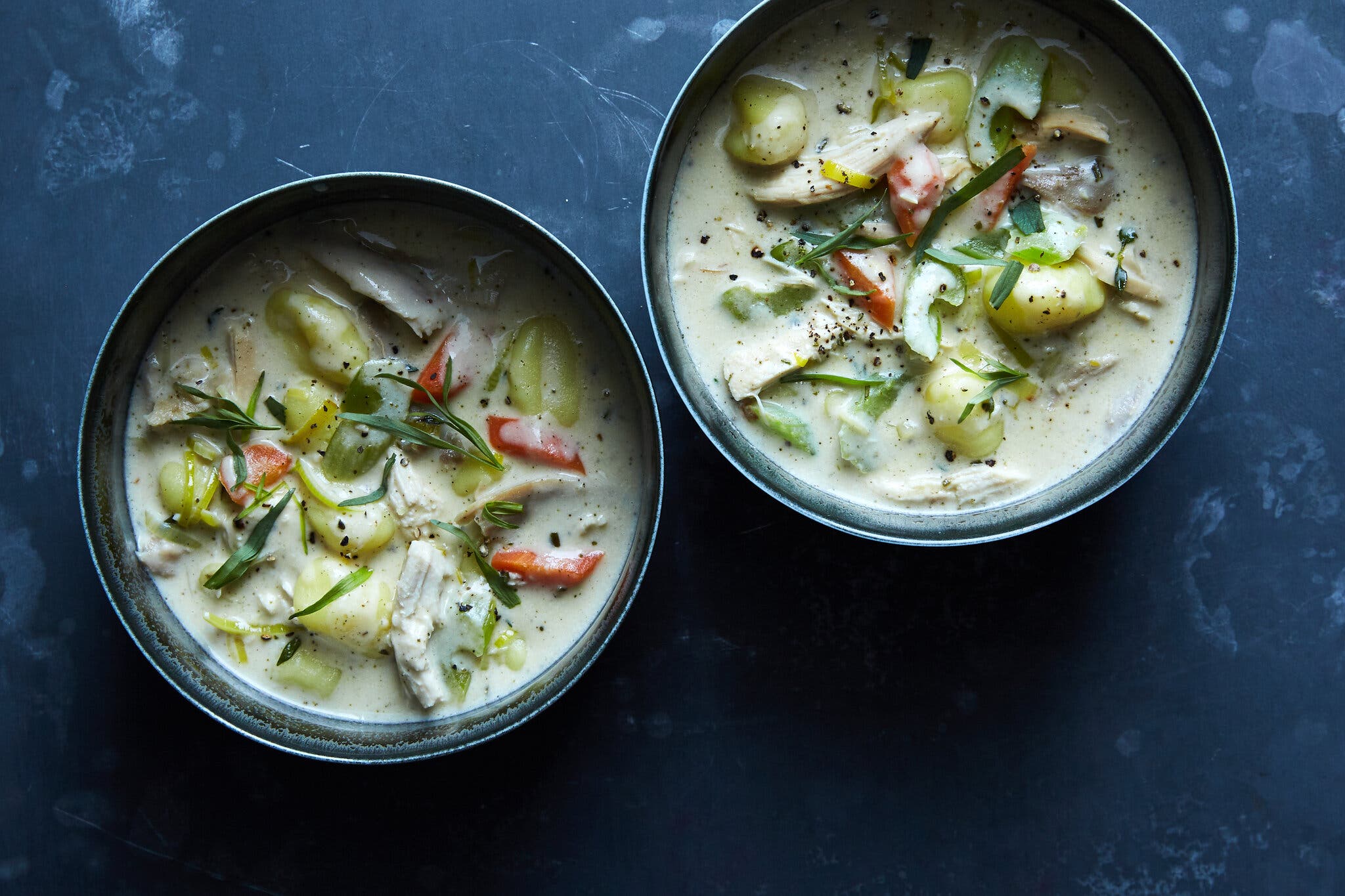 An overhead shot of two bowls of chicken and dumpling soup, on a navy blue countertop.