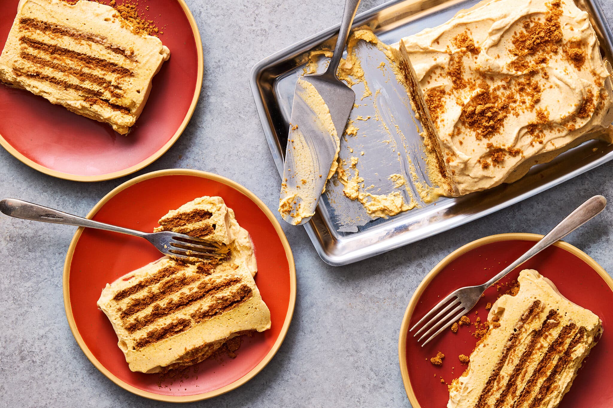 An overhead image of a pumpkin icebox cake in a pan. Around it, three red plates with slices of cake.