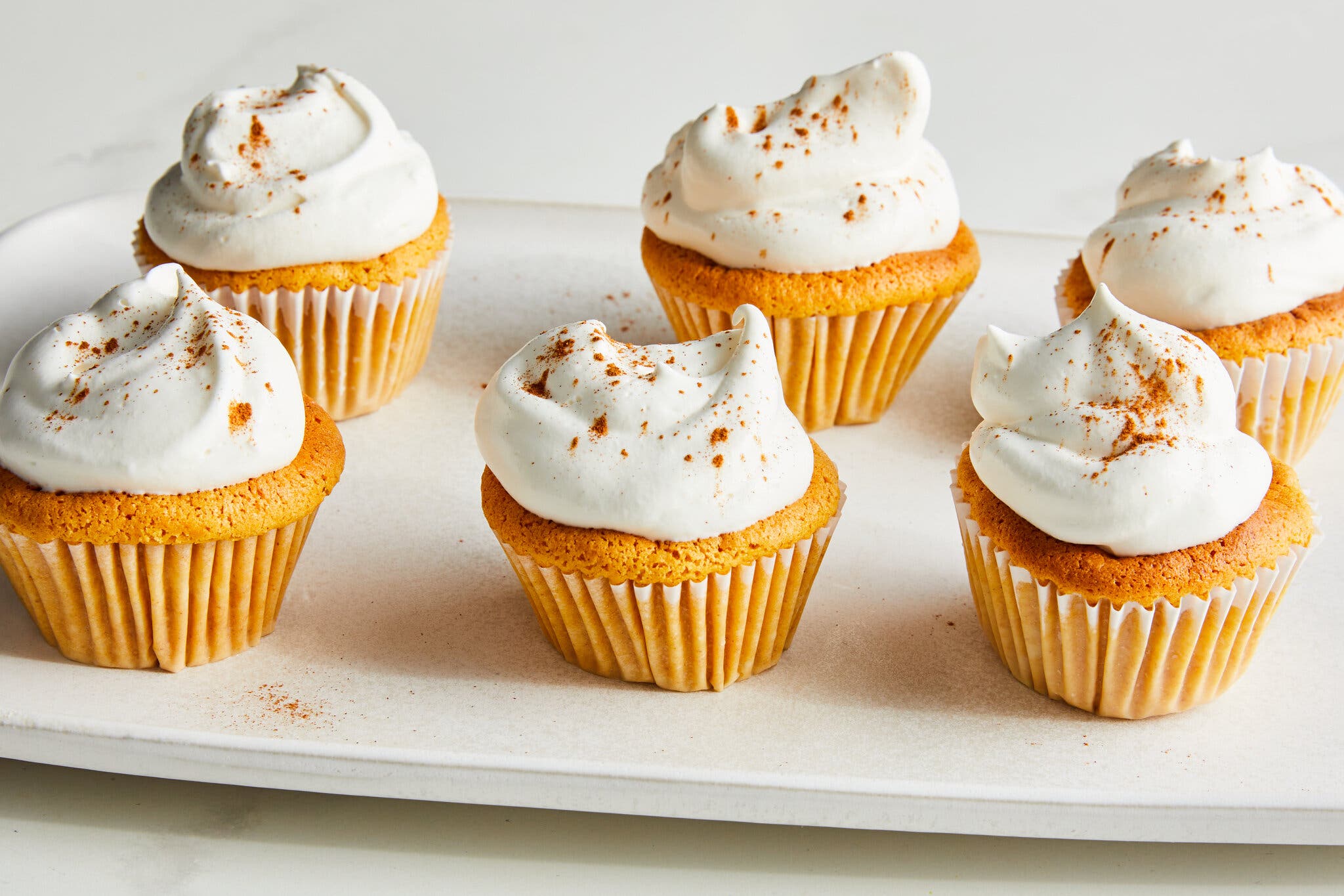 A side shot of a plate of six mini cupcake-size pumpkin spice cheesecakes.
