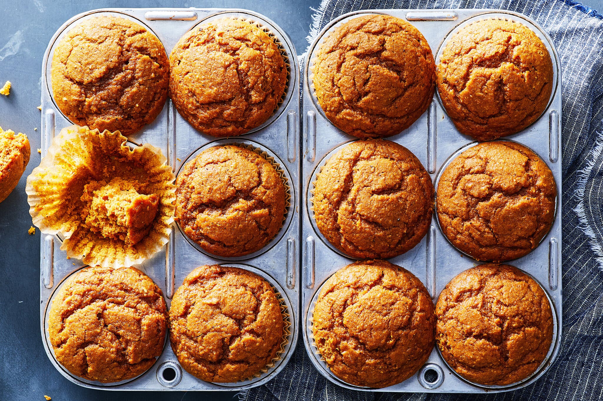 An overhead image of a dozen pumpkin maple muffins in muffin tins. Part of one of the muffins has been eaten.