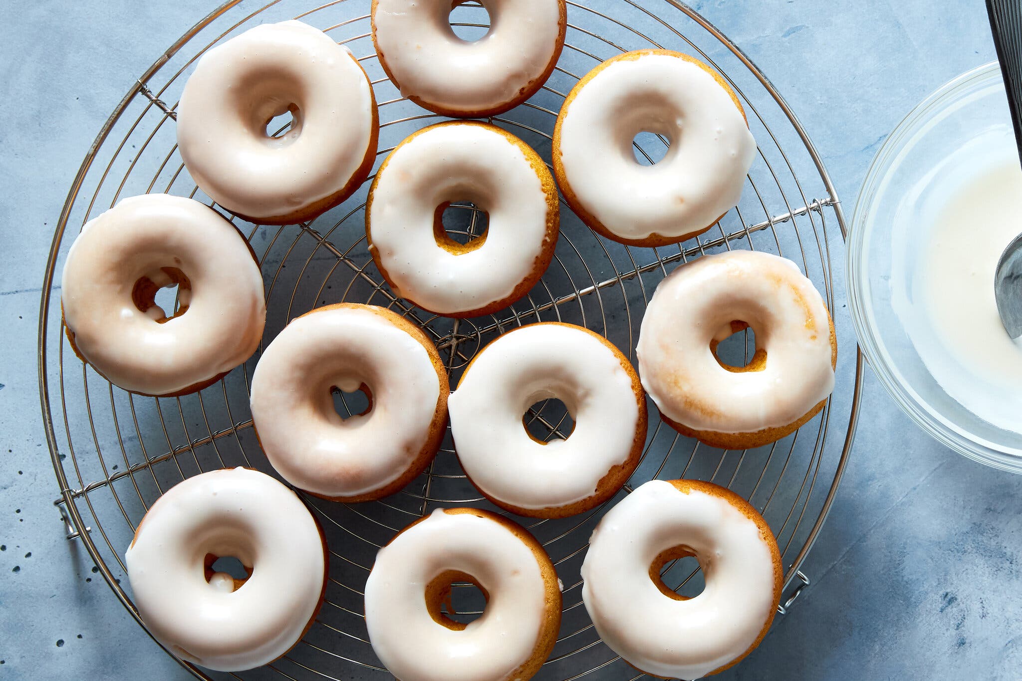 An overhead image of 11 glazed pumpkin doughnuts on a cooling rack.